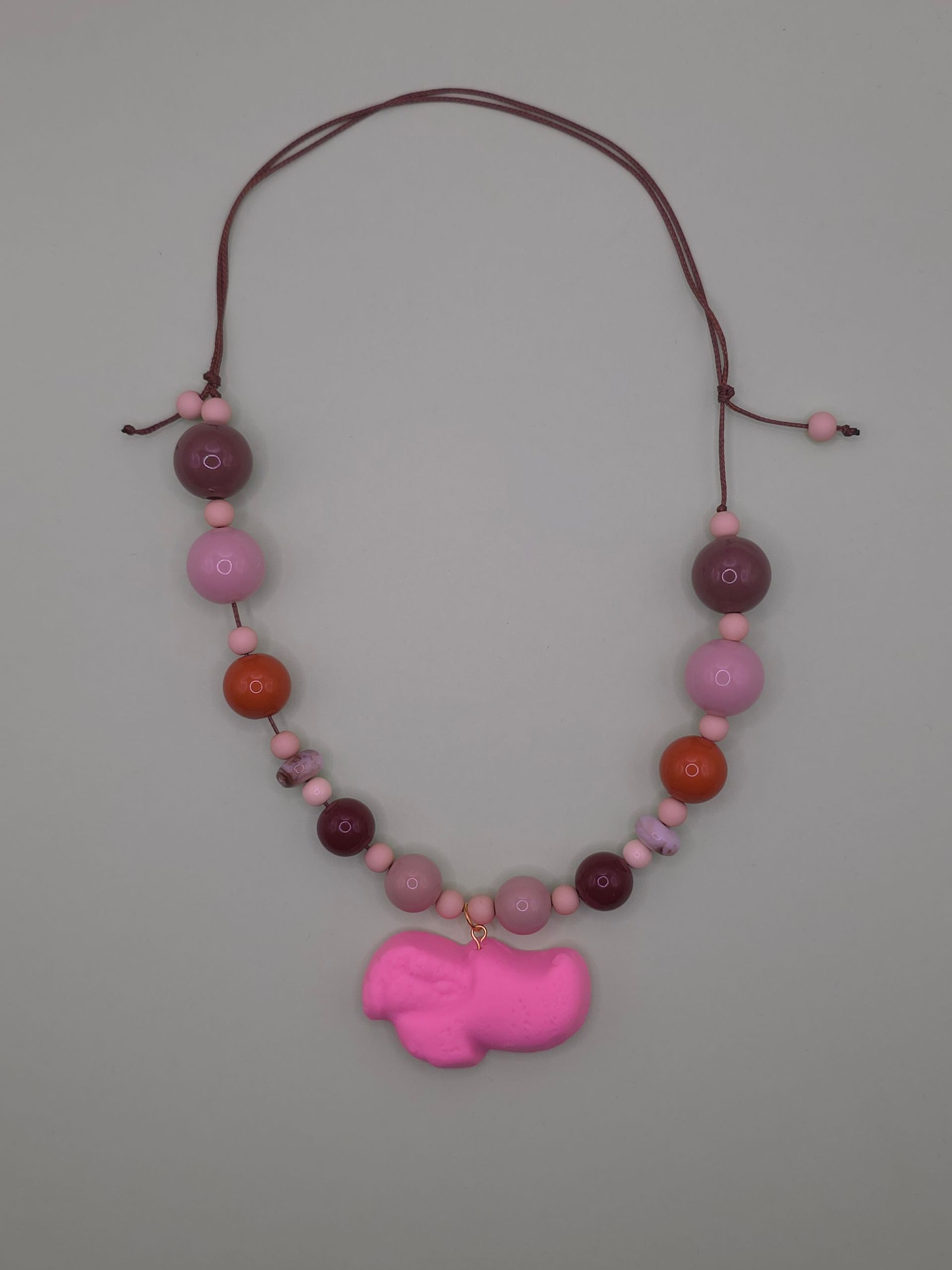 Roze kralenketting met een grote, felroze hanger op een witte achtergrond.