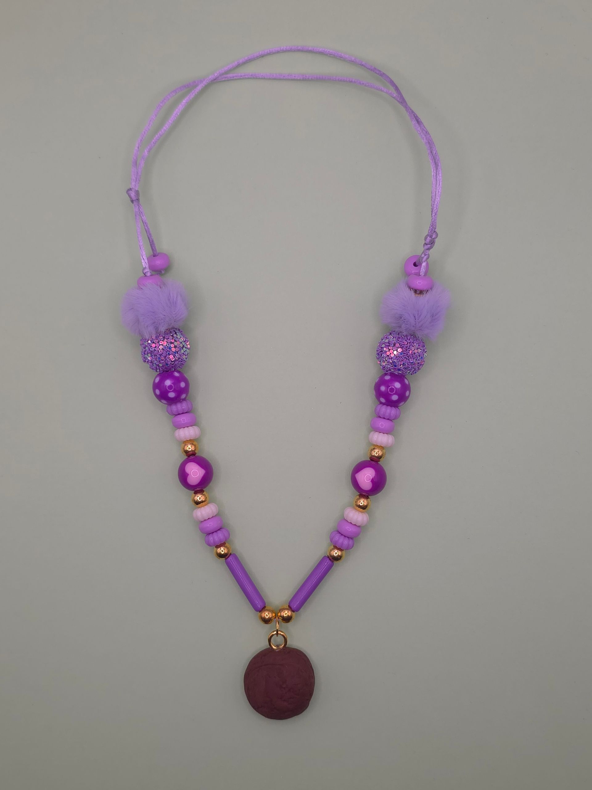 Paarse kralenketting met hartvormige bedeltjes en een ronde hanger op een lichte achtergrond.