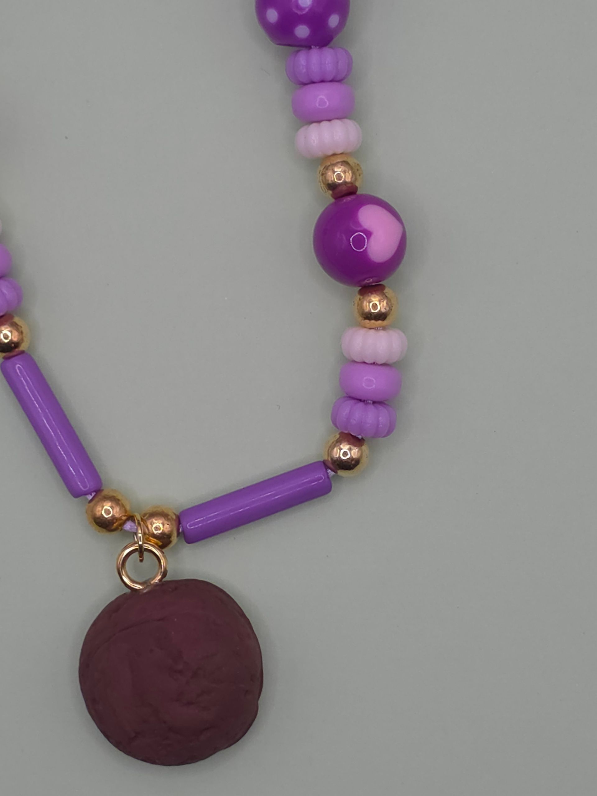 Paarse kralenketting met hartvormige bedeltjes en een ronde hanger op een lichte achtergrond.