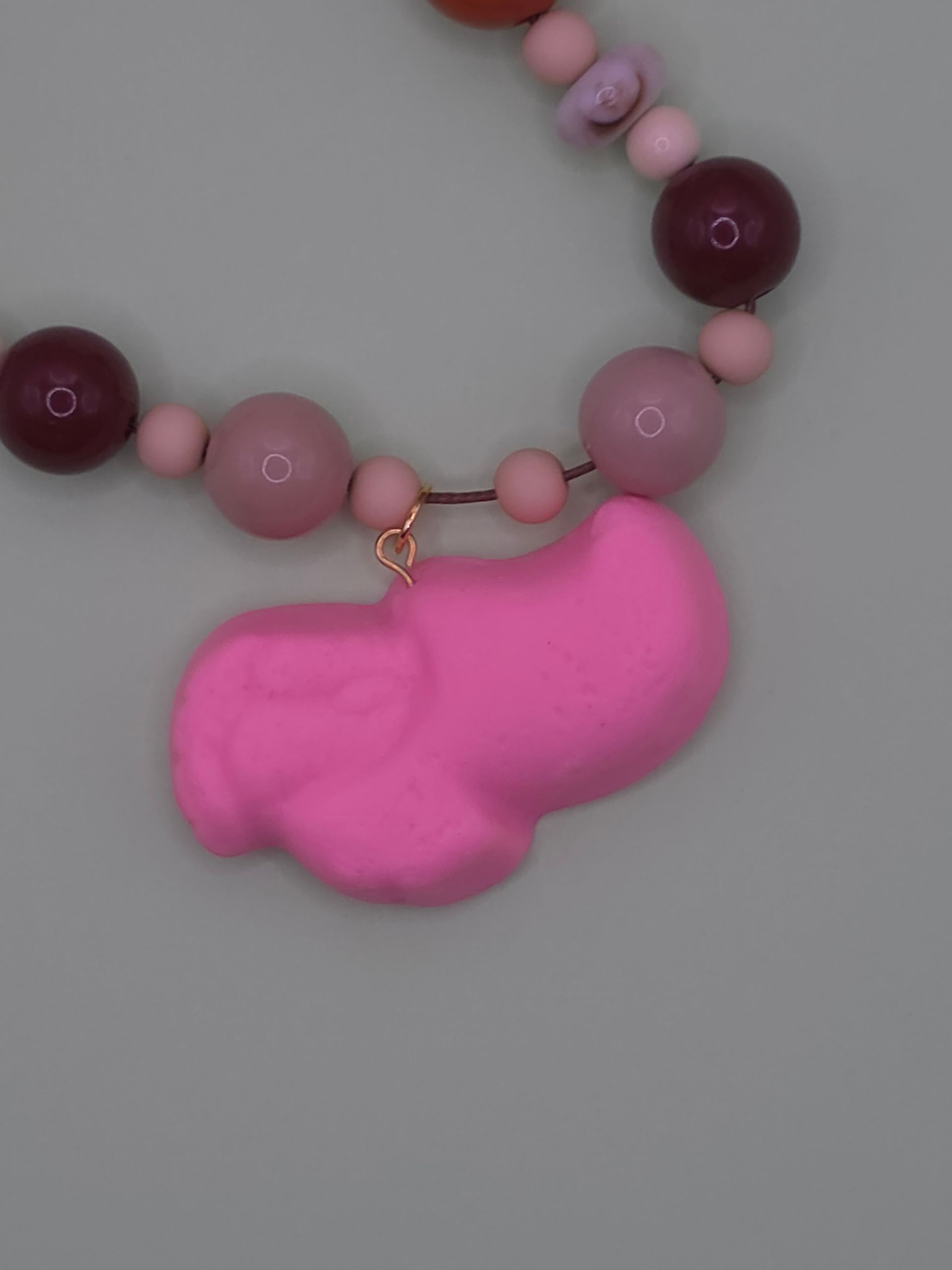 Roze kralenketting met een grote, felroze hanger op een witte achtergrond.
