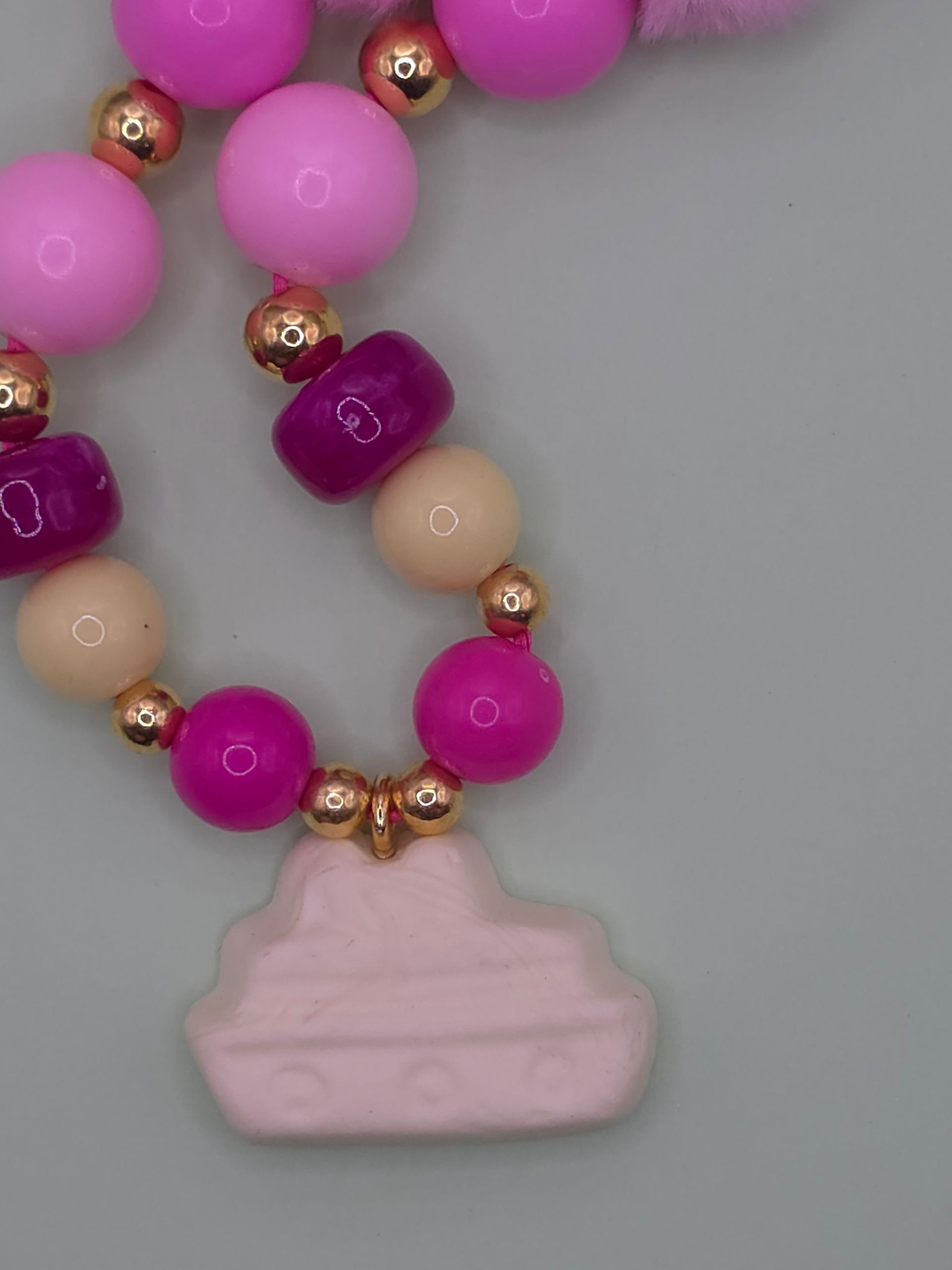 Roze kralenketting met een lichtroze hanger op een grijze achtergrond.