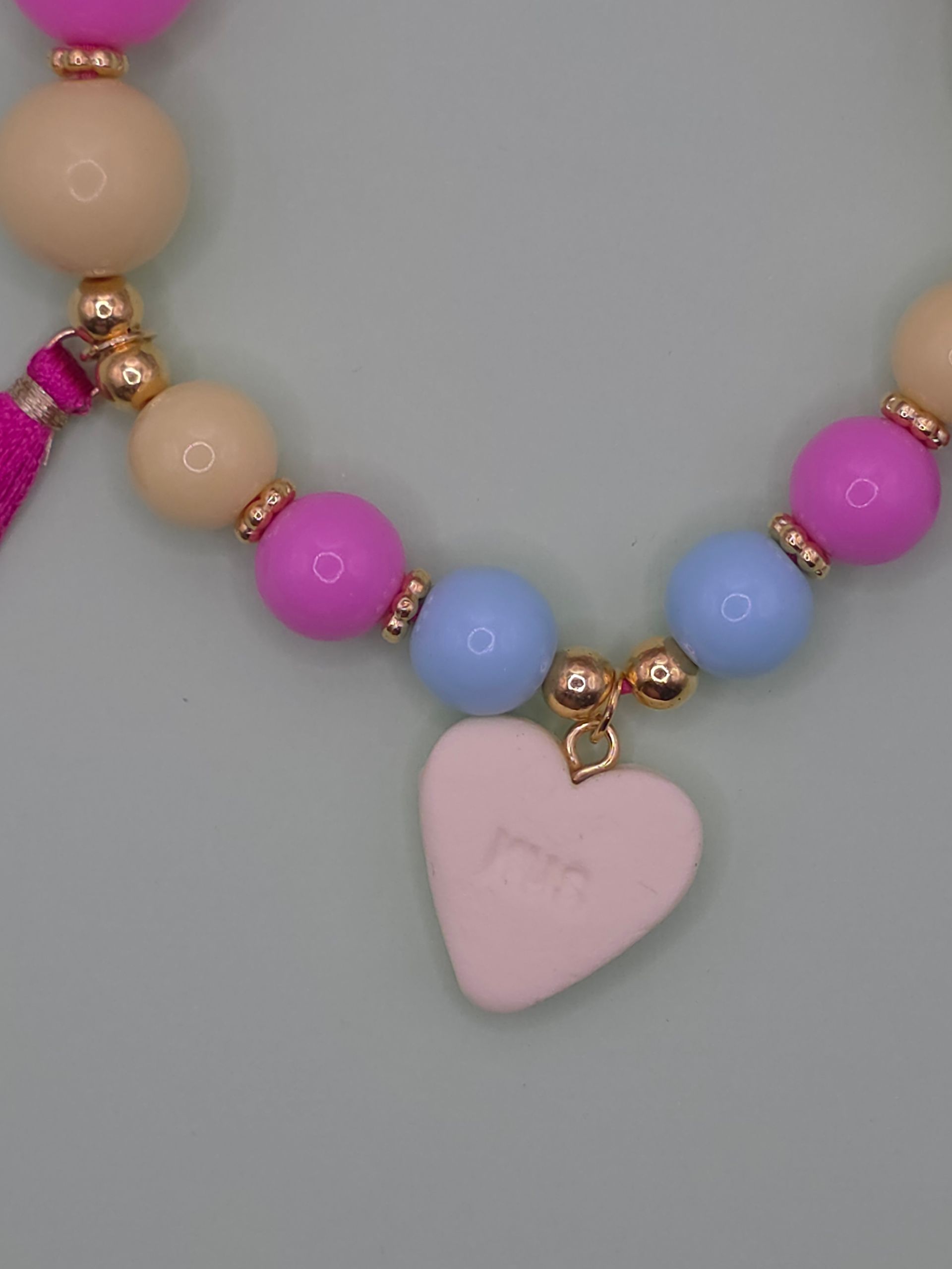 Roze kralenketting met hartvormige hanger en bungelende kwastjes op een witte achtergrond.