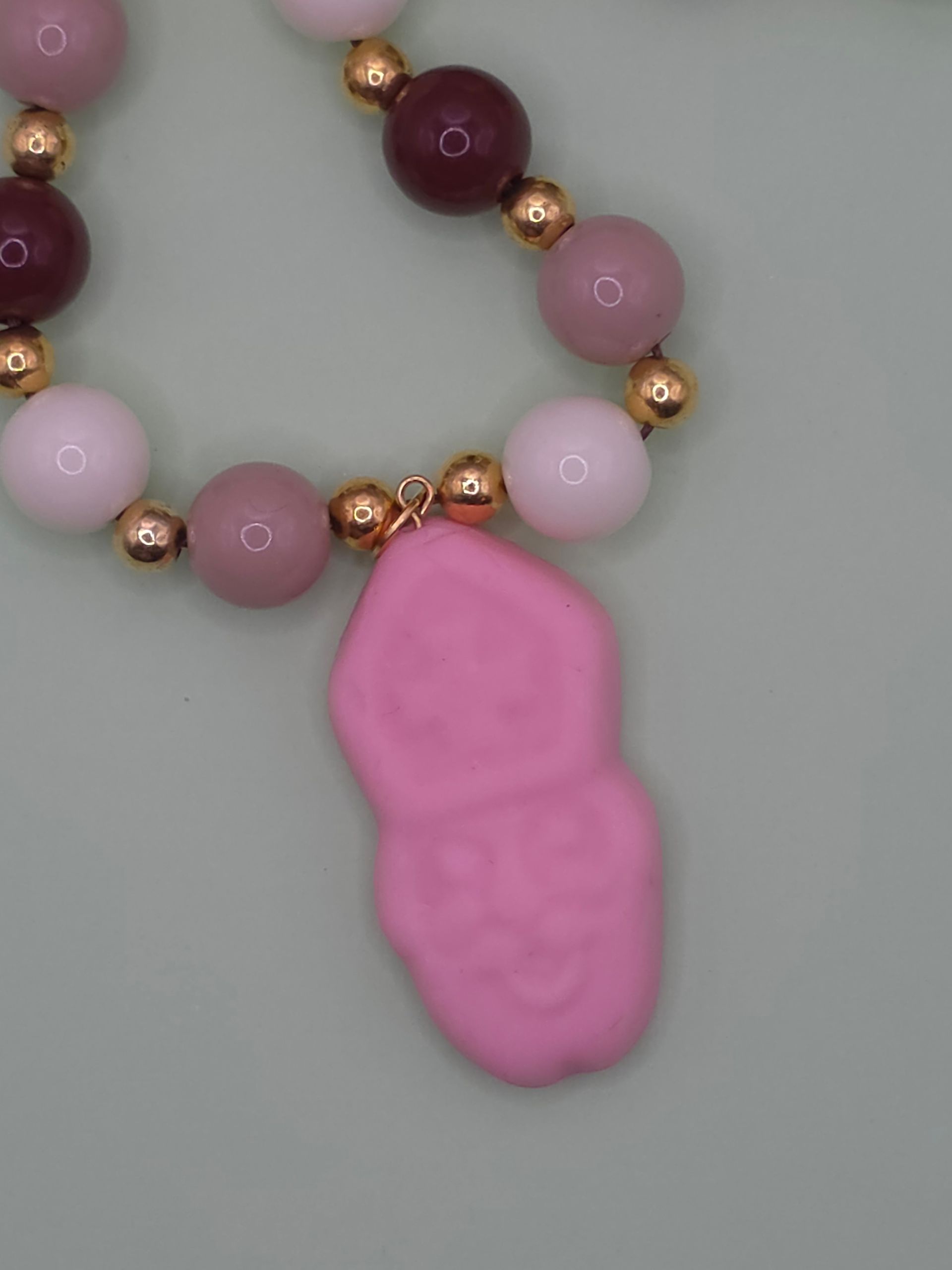 Roze hanger in de vorm van een poot aan een kralenketting met roze, bordeauxrode en gouden kralen.