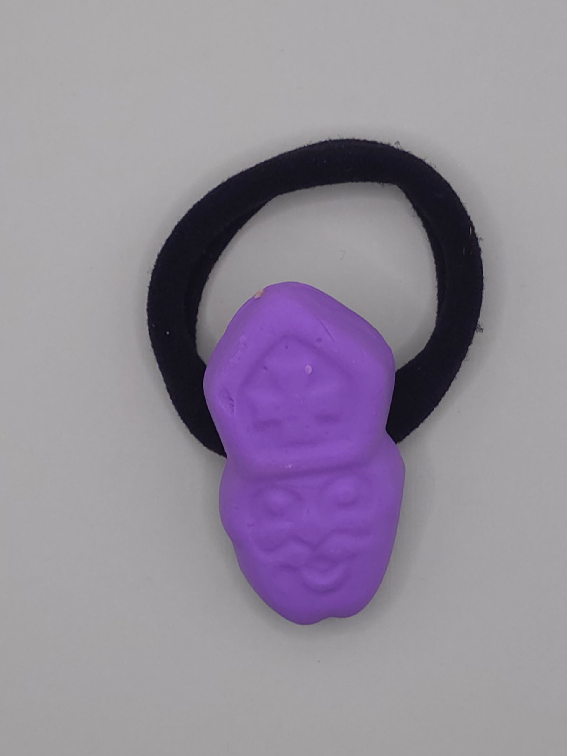 Paars bijvormig speeltje op een ring, omringd door verspreide rode en pastelkleurige kralen op een lichte achtergrond.