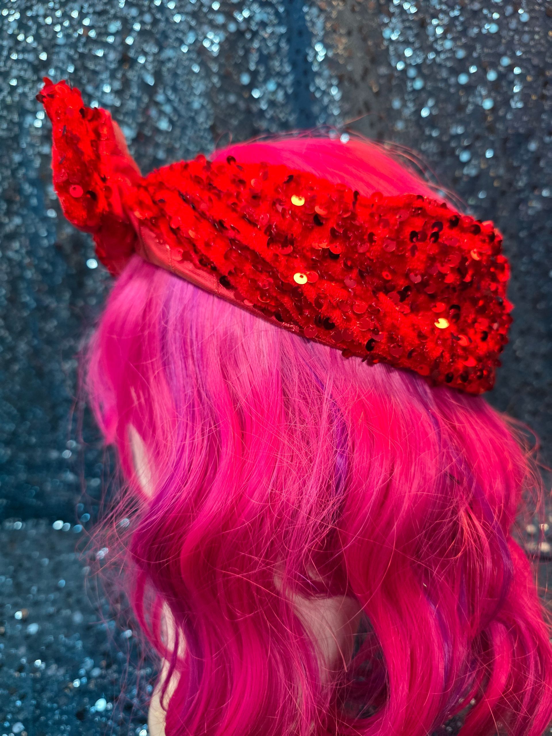 Etalagepoppenhoofd met een felroze pruik en een rode paillettenstrik tegen een glitterende blauwe achtergrond
