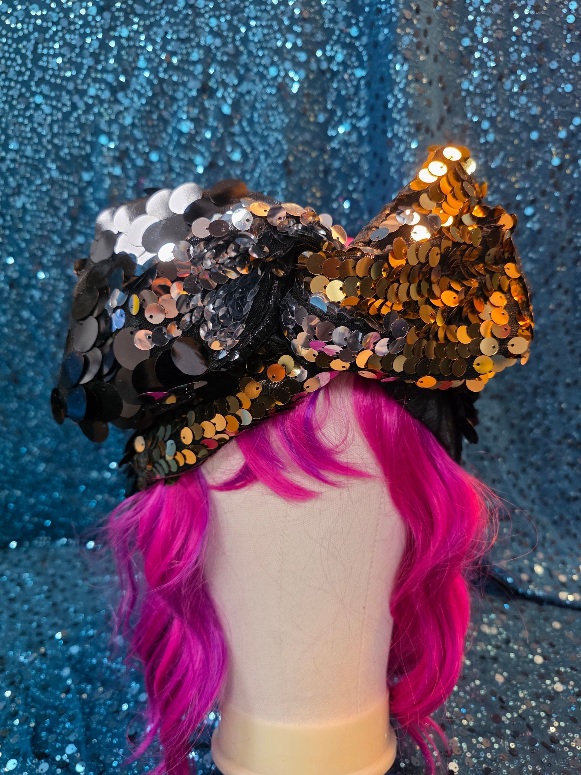 Etalagepoppenhoofd met felroze pruik en zwart-oranje hoed met paillettenstrik, op een blauwe glitterachtergrond