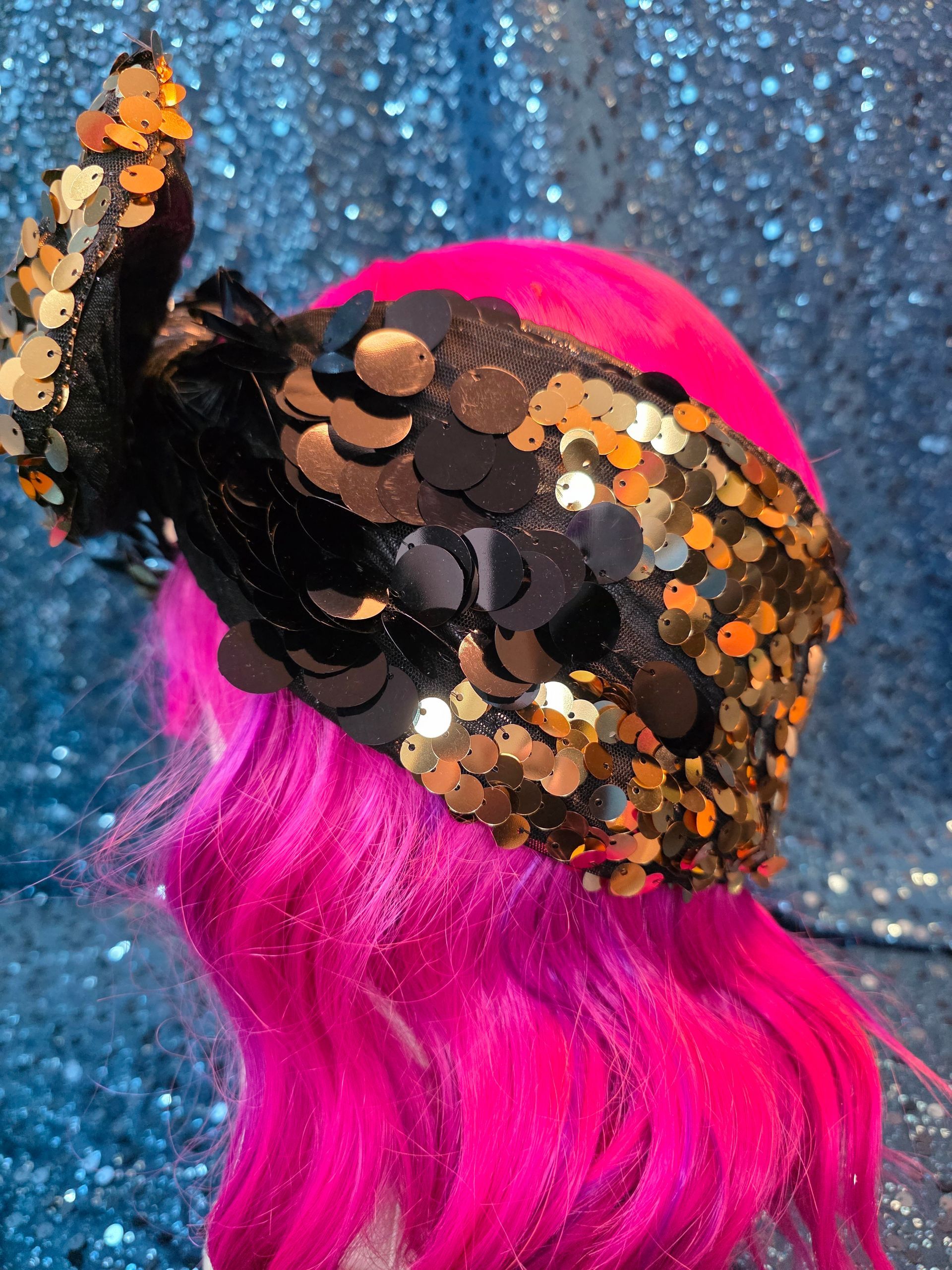Etalagepoppenhoofd met felroze pruik en zwart-oranje hoed met paillettenstrik, op een blauwe glitterachtergrond