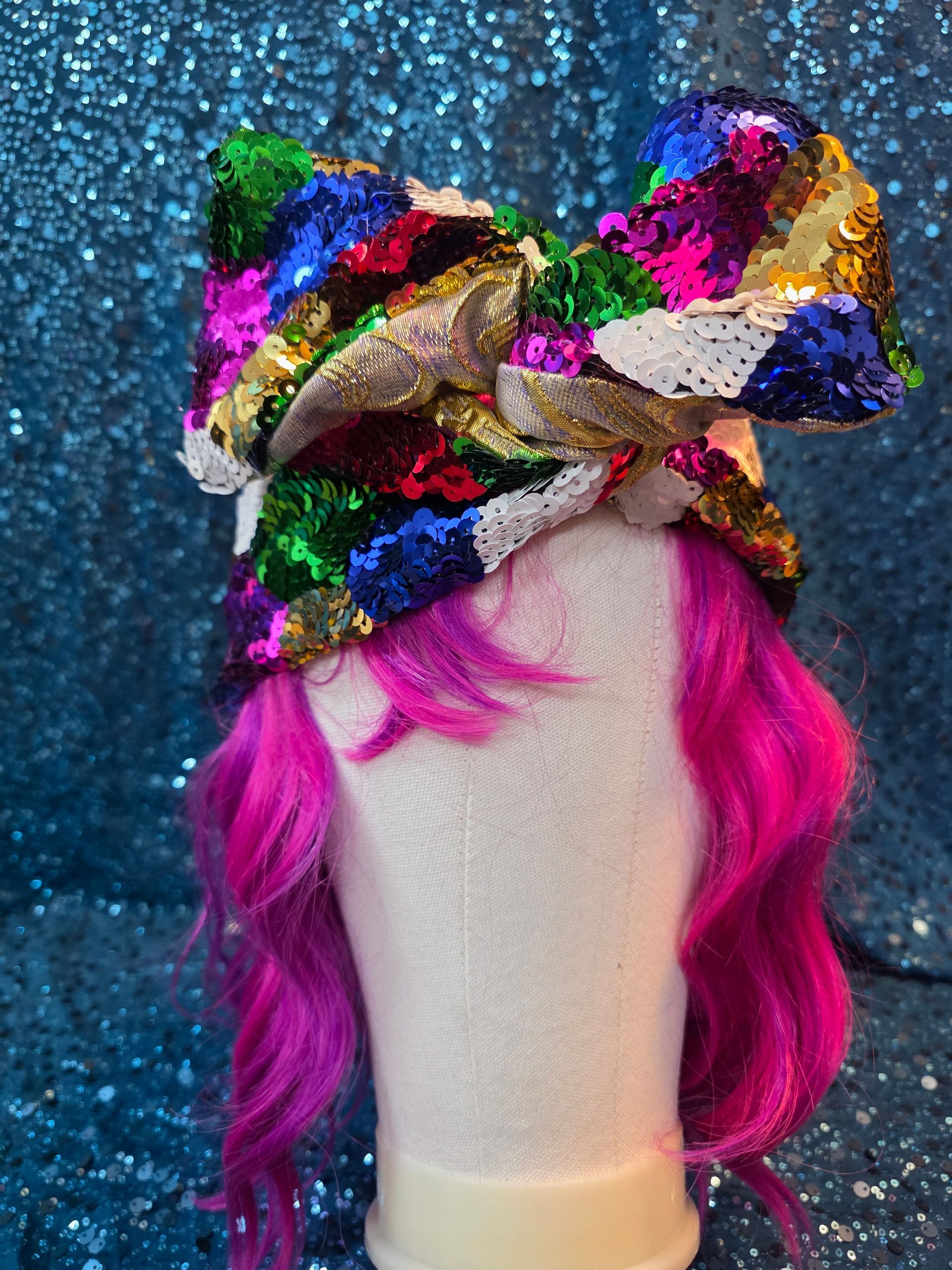 Kleurrijke hoofddoek met pailletten op een paspoppenhoofd met felroze haar tegen een glinsterende blauwe achtergrond