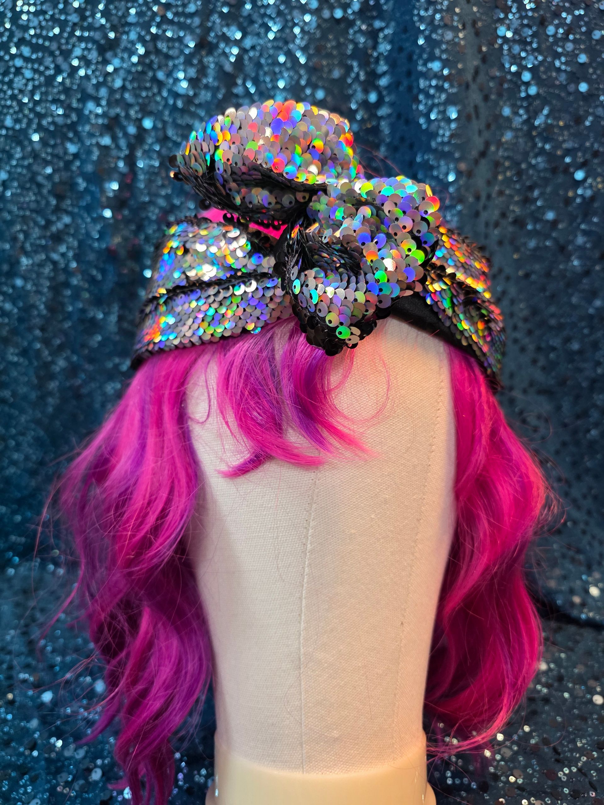Etalagepop met felroze haar en een veelkleurige pailletten-tulband tegen een blauwe glitterachtergrond