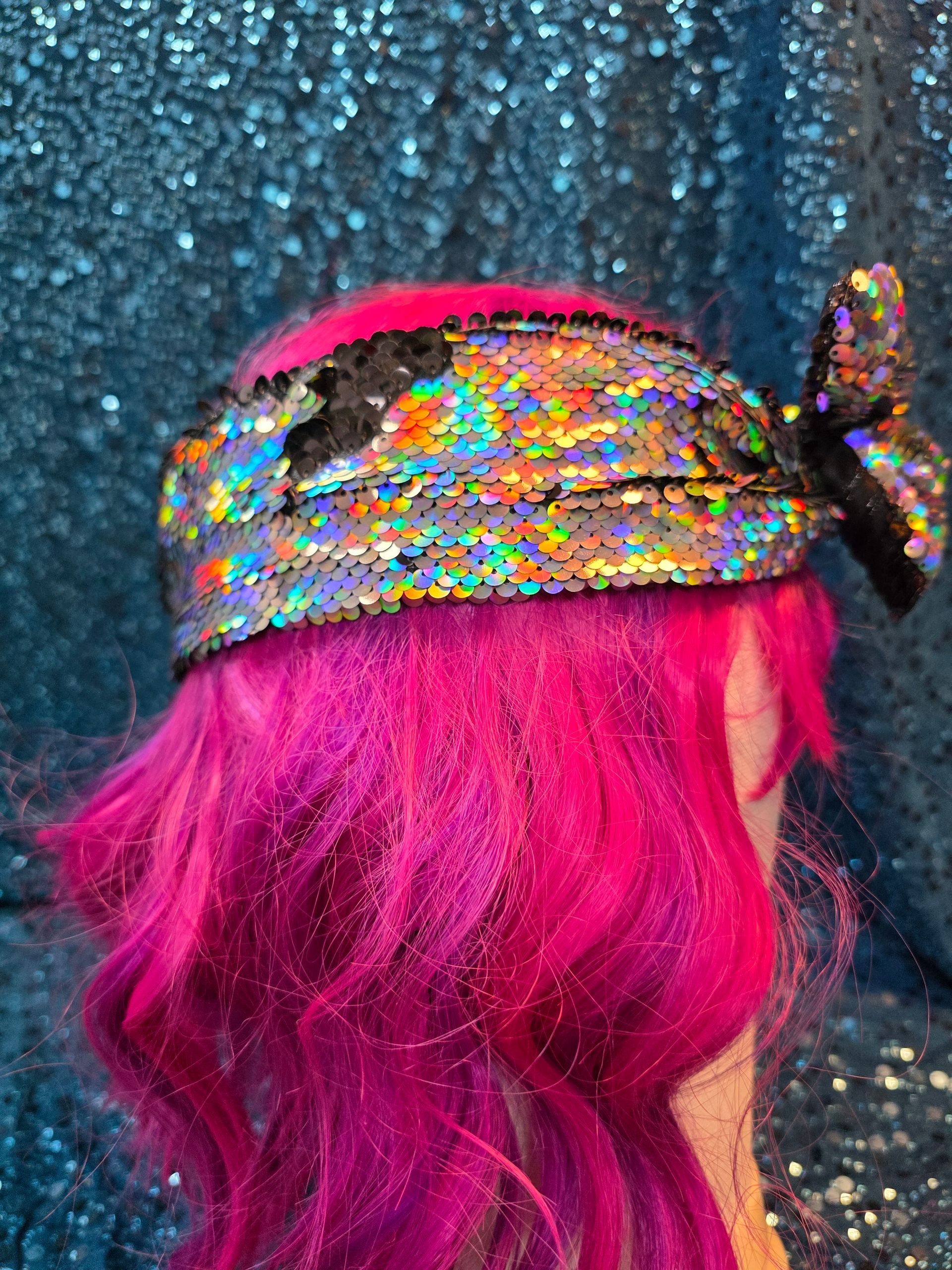 Etalagepop met felroze haar en een veelkleurige pailletten-tulband tegen een blauwe glitterachtergrond