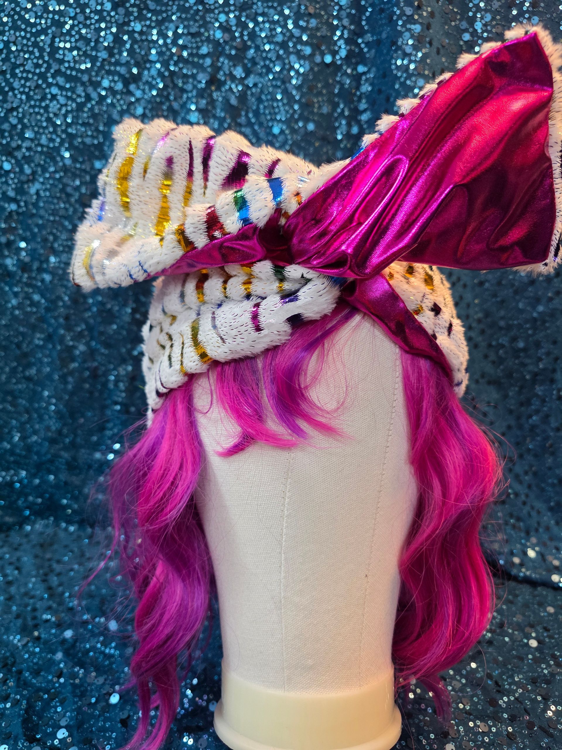 Etalagepoppenhoofd met wit wollen haar, een felroze strik en een blauwe glitterachtergrond