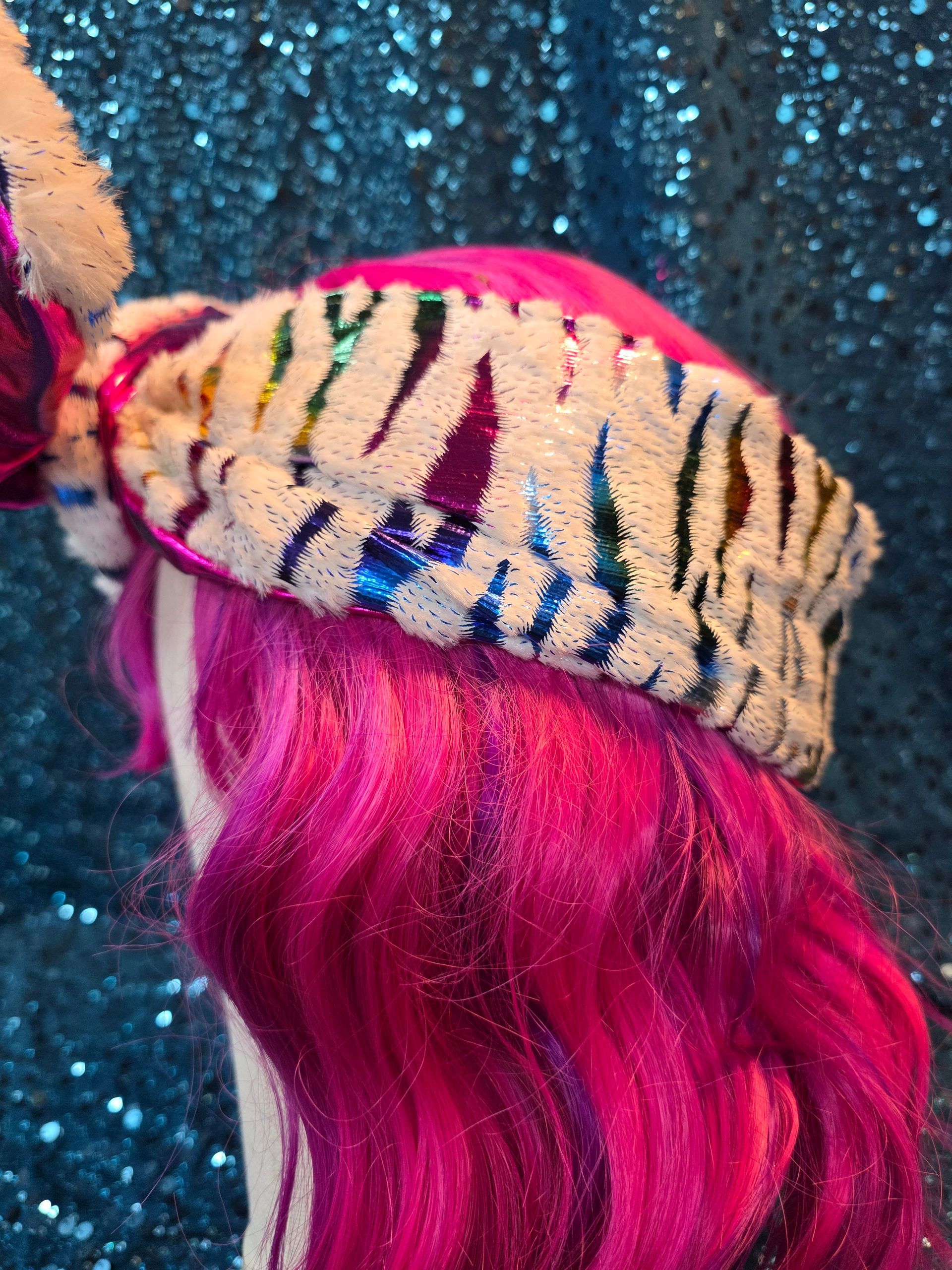 Etalagepoppenhoofd met wit wollen haar, een felroze strik en een blauwe glitterachtergrond