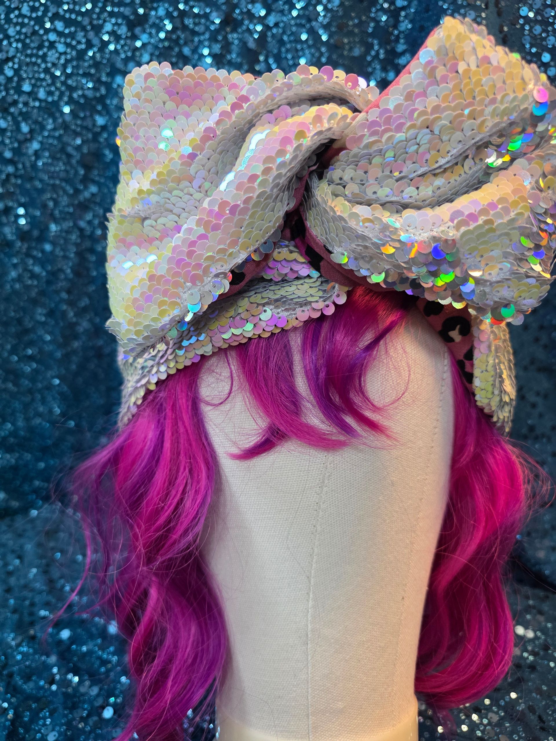 Sprankelend rozegouden strikhoofddeksel op een paspophoofd met felmagenta haar tegen een glinsterende blauwe achtergrond