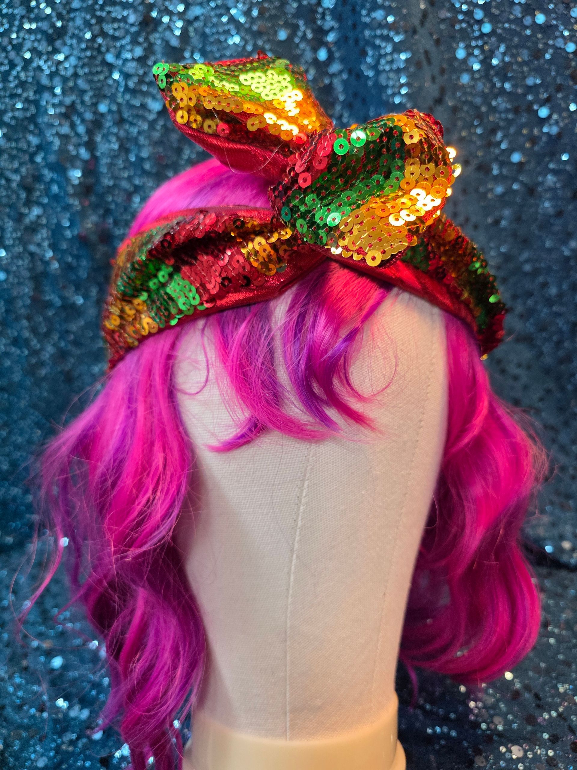 Etalagepoppenhoofd met felroze haar en een veelkleurige strik met pailletten tegen een blauwe glitterachtergrond
