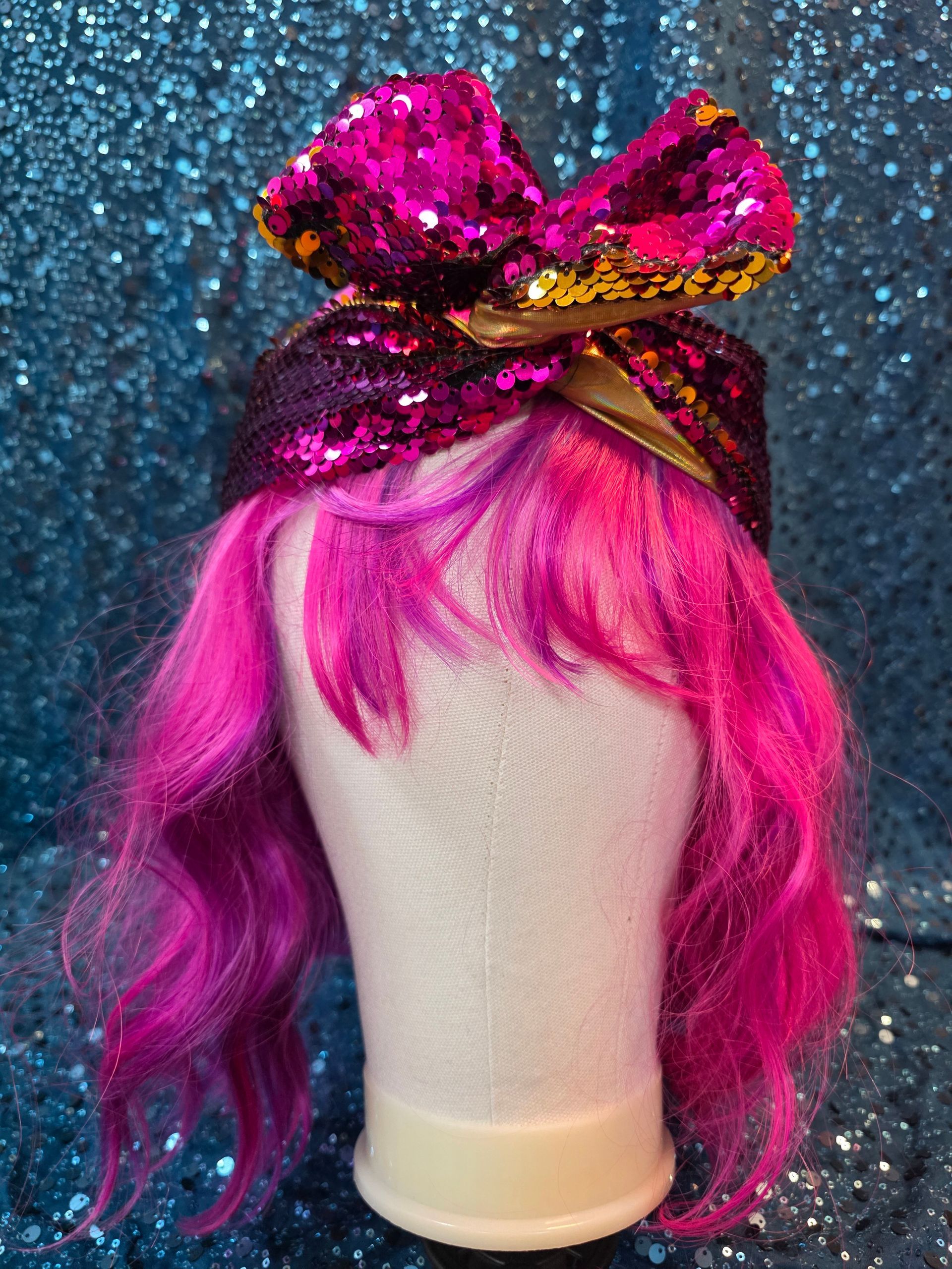 Etalagepophoofd met een felroze pruik en een glanzende magenta strik tegen een glitterende blauwe achtergrond