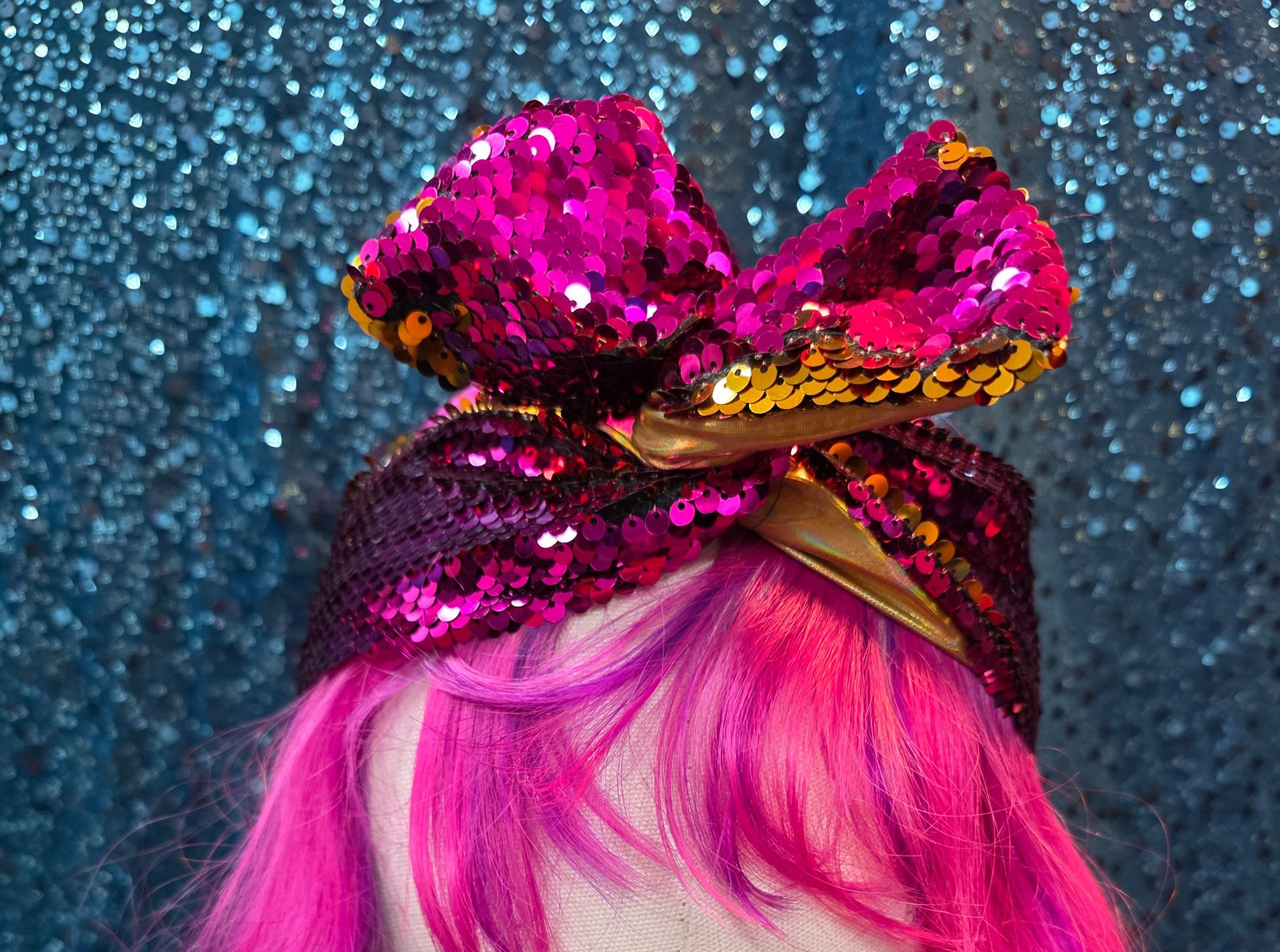 Felroze haar onder een sprankelende magenta strik tegen een glitterende blauwe achtergrond