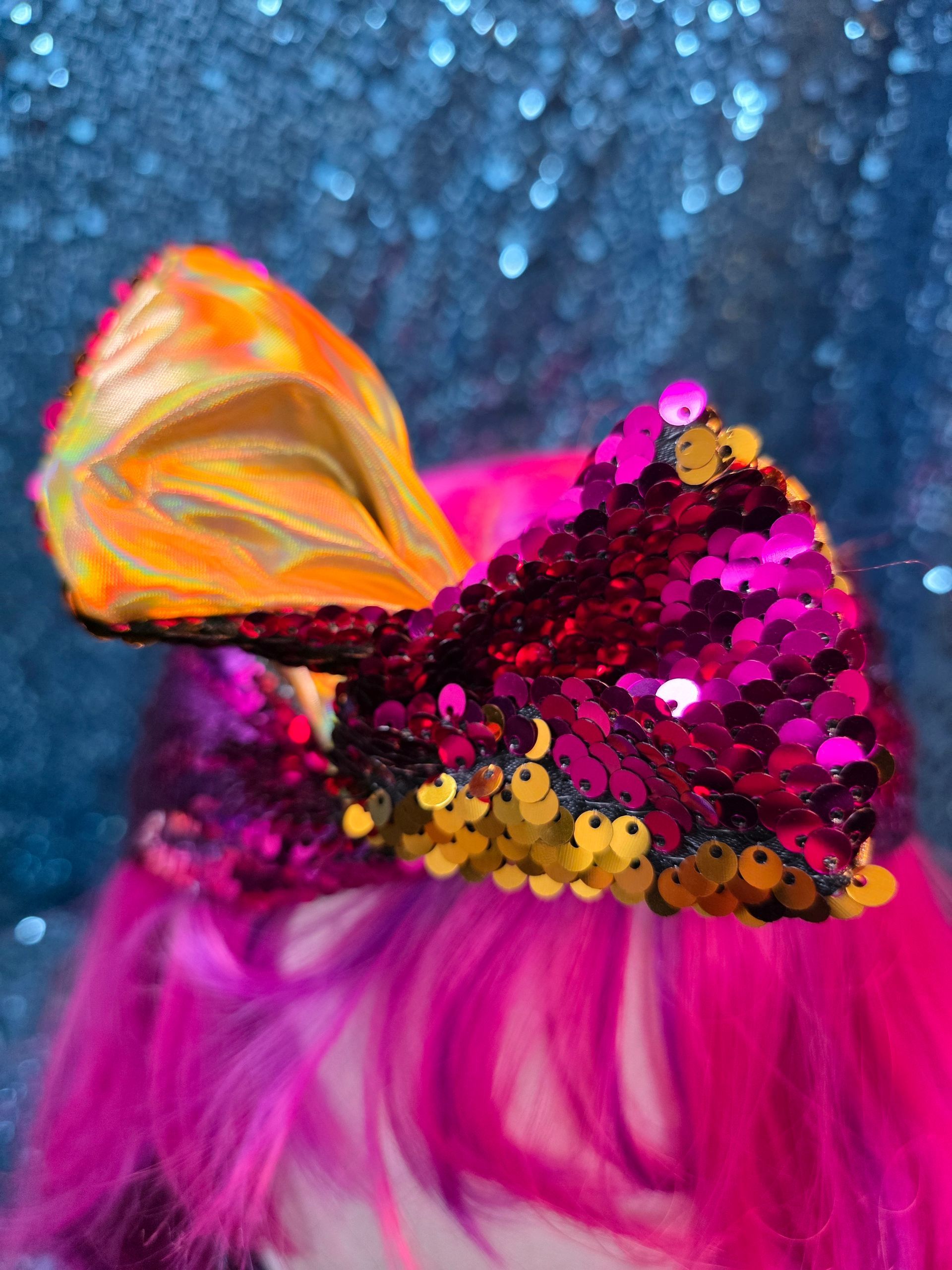 Etalagepophoofd met een felroze pruik en een glanzende magenta strik tegen een glitterende blauwe achtergrond