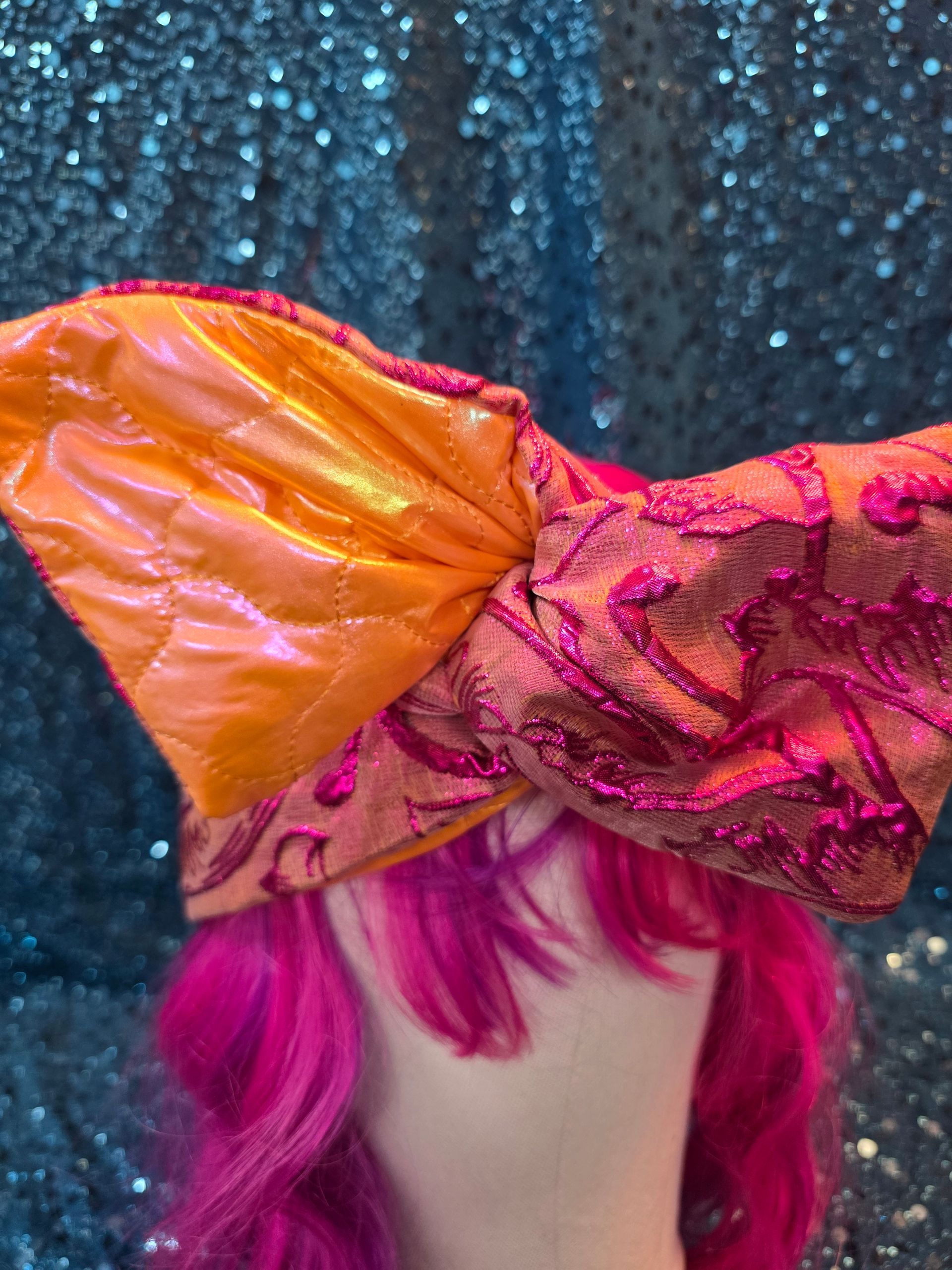 Paspop met felroze pruik en oranje strik met patroon tegen een blauwe glitterachtergrond