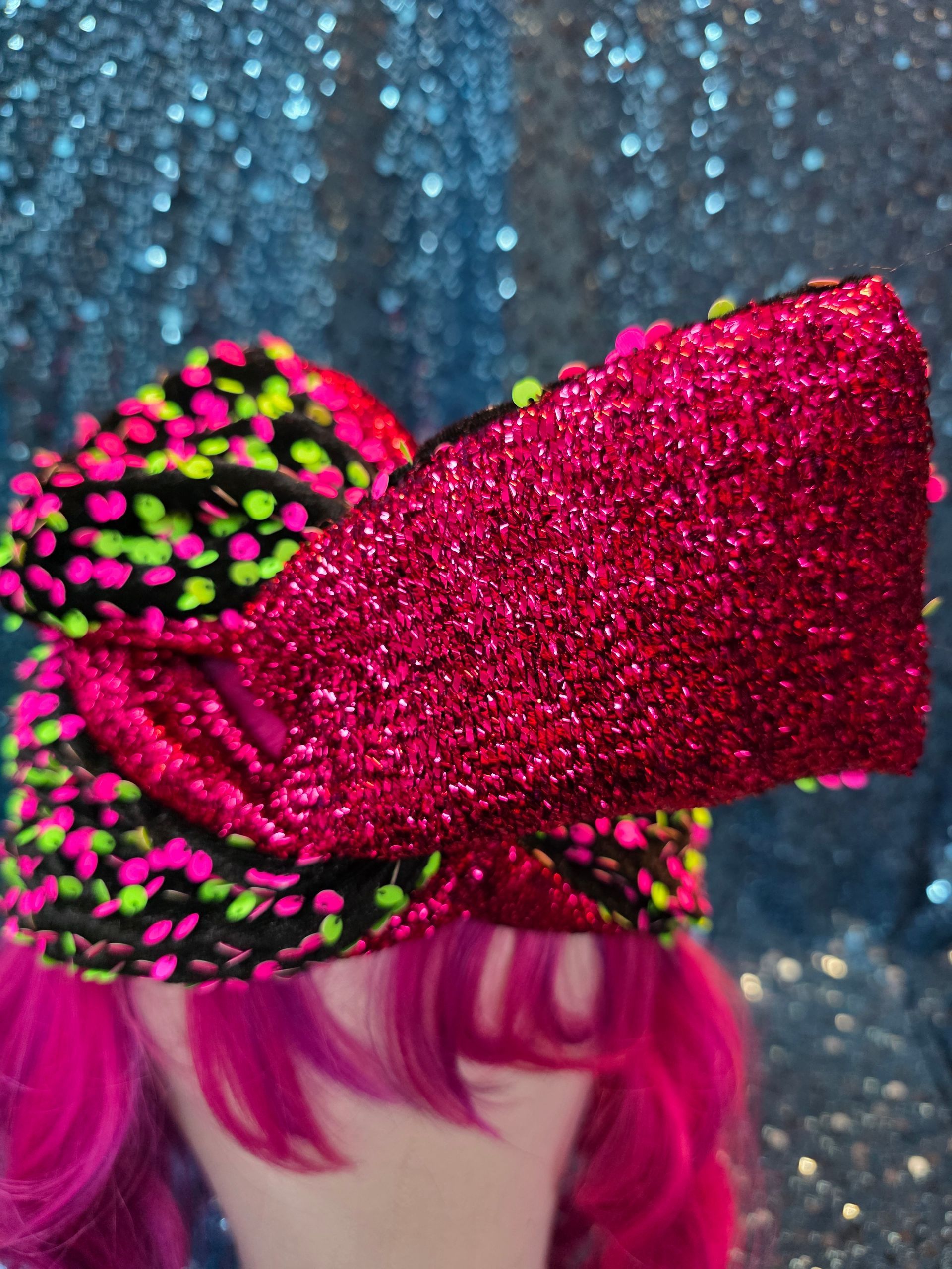 Etalagepophoofd met een felroze pruik en een zwarte gebloemde tulbandhoofdband op een blauwe glitterachtergrond