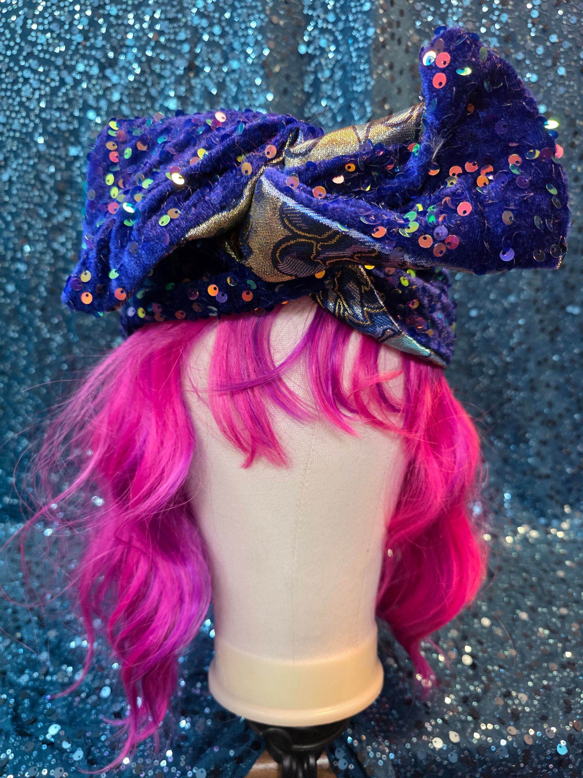 Etalagepoppenhoofd met felroze pruik en grote donkerblauwe strik met pailletten op een glitterende achtergrond