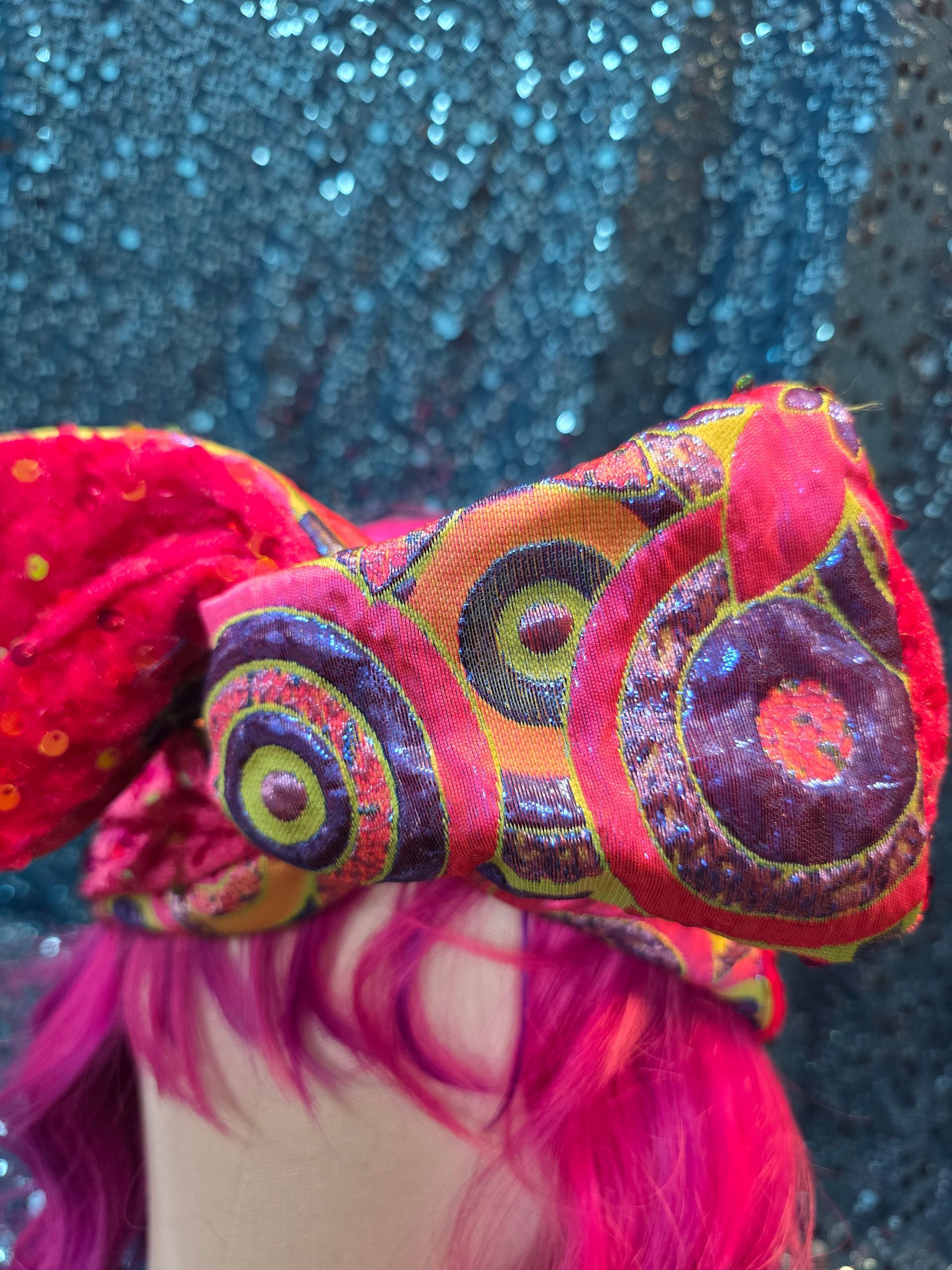 Close-up van een kleurrijke uilenmuts met een patroon, boven felroze haar tegen een blauwe glitterachtergrond