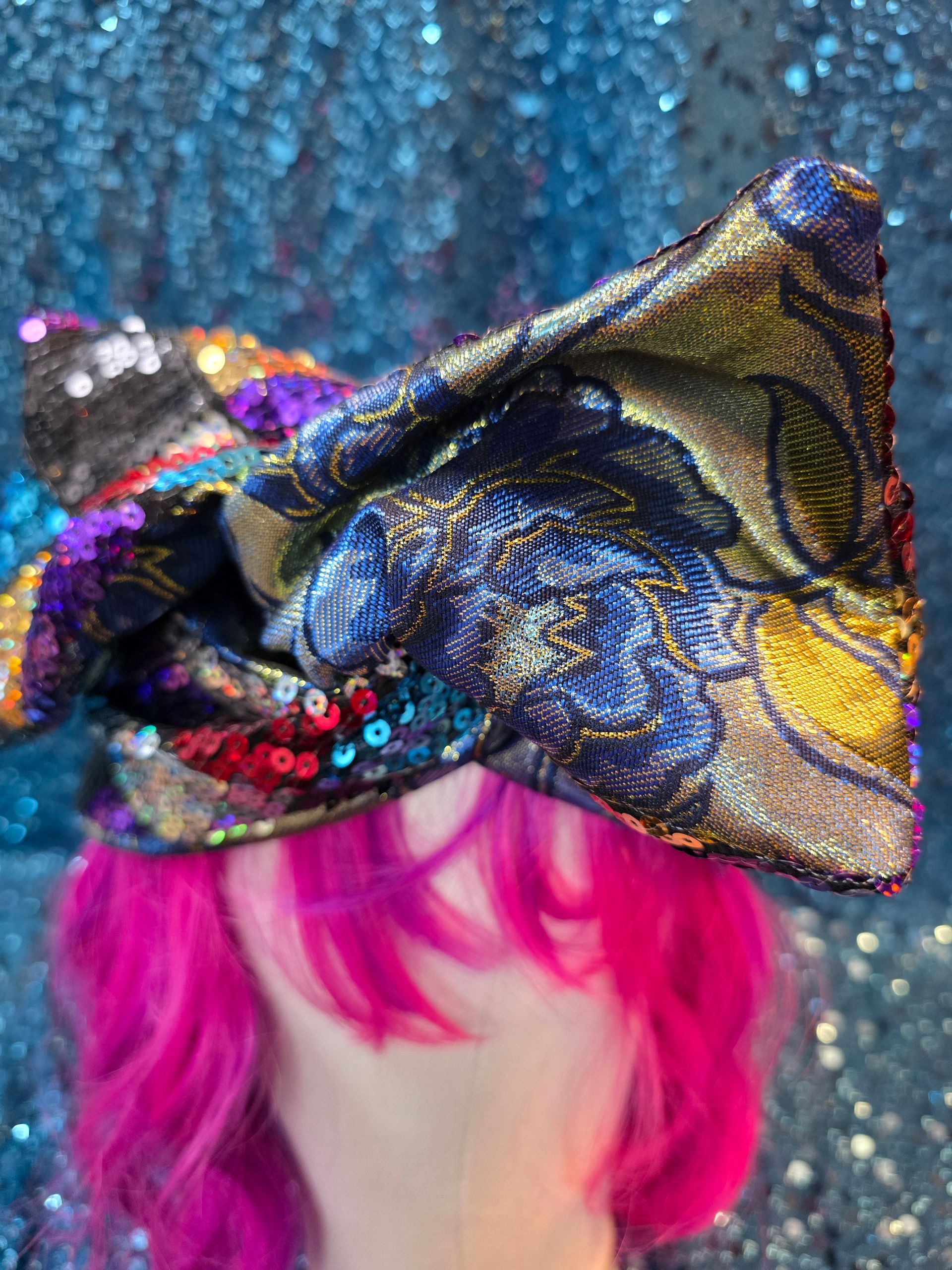 Veelkleurige strik met pailletten op een felroze pruik op een paspophoofd tegen een glitterende blauwe achtergrond