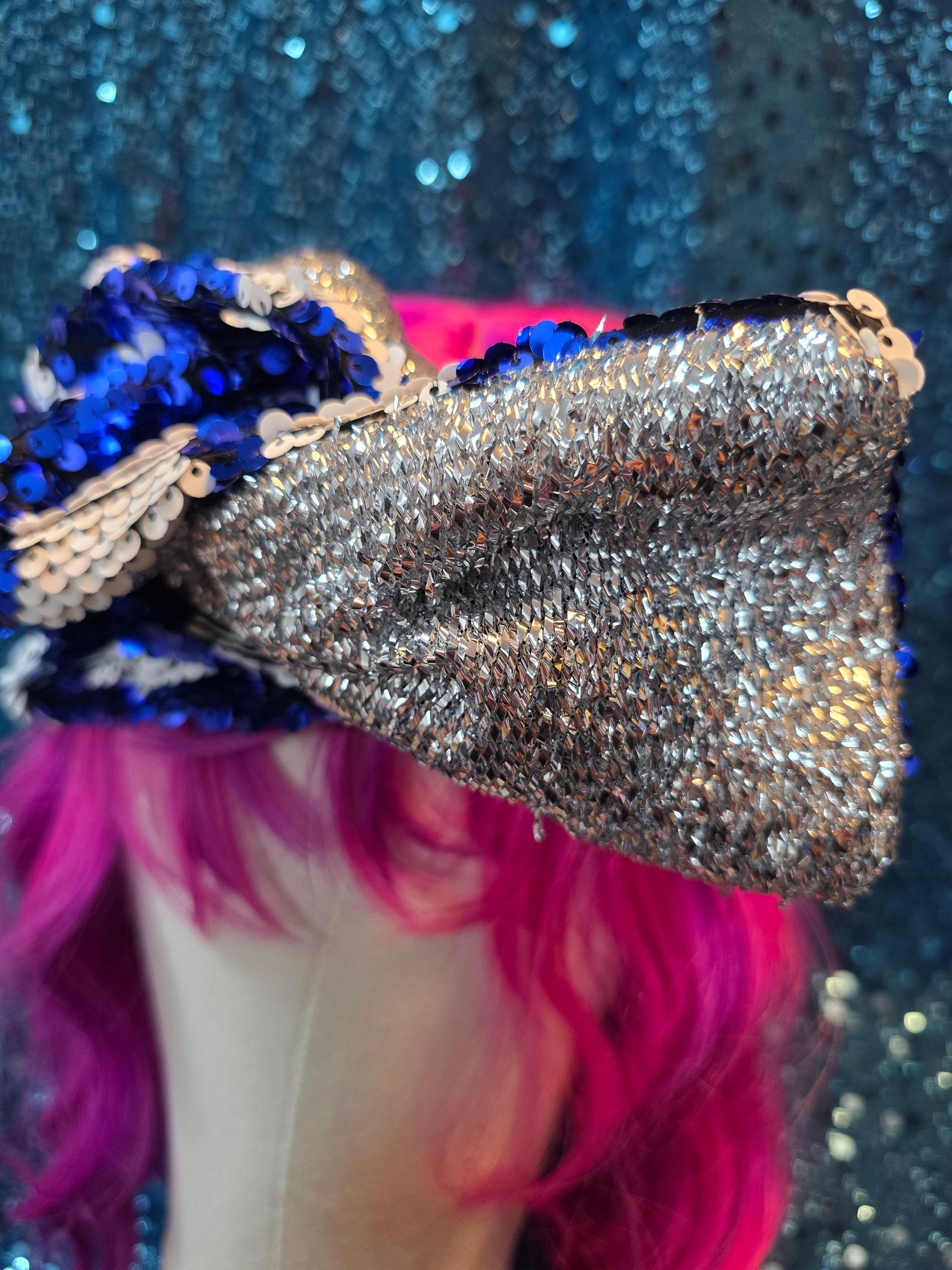 Etalagepoppenhoofd met een felroze pruik en een grote blauwe strik met pailletten op een glitterende achtergrond
