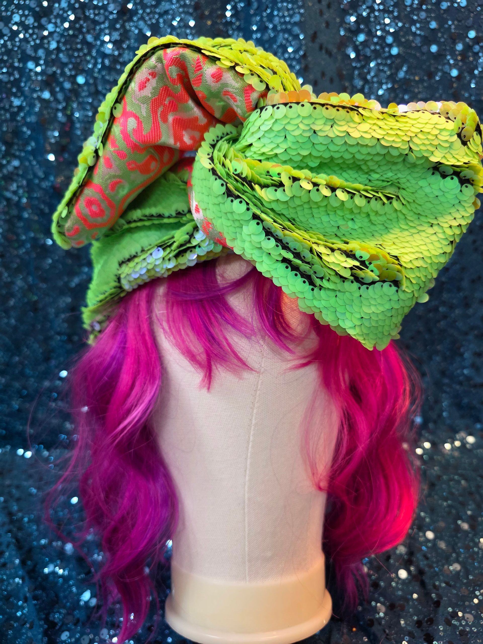 Etalagepoppenhoofd met neonroze haar en een grote groen-gele bloemenstrik als hoofddeksel
