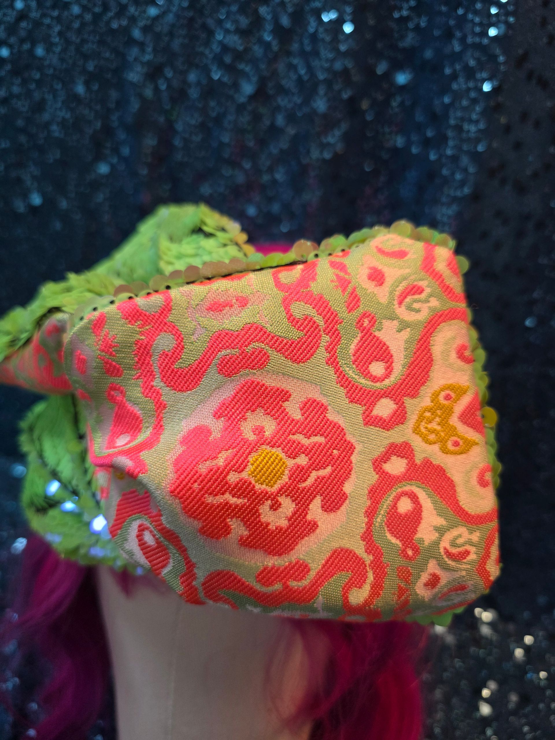 Etalagepoppenhoofd met neonroze haar en een grote groen-gele bloemenstrik als hoofddeksel