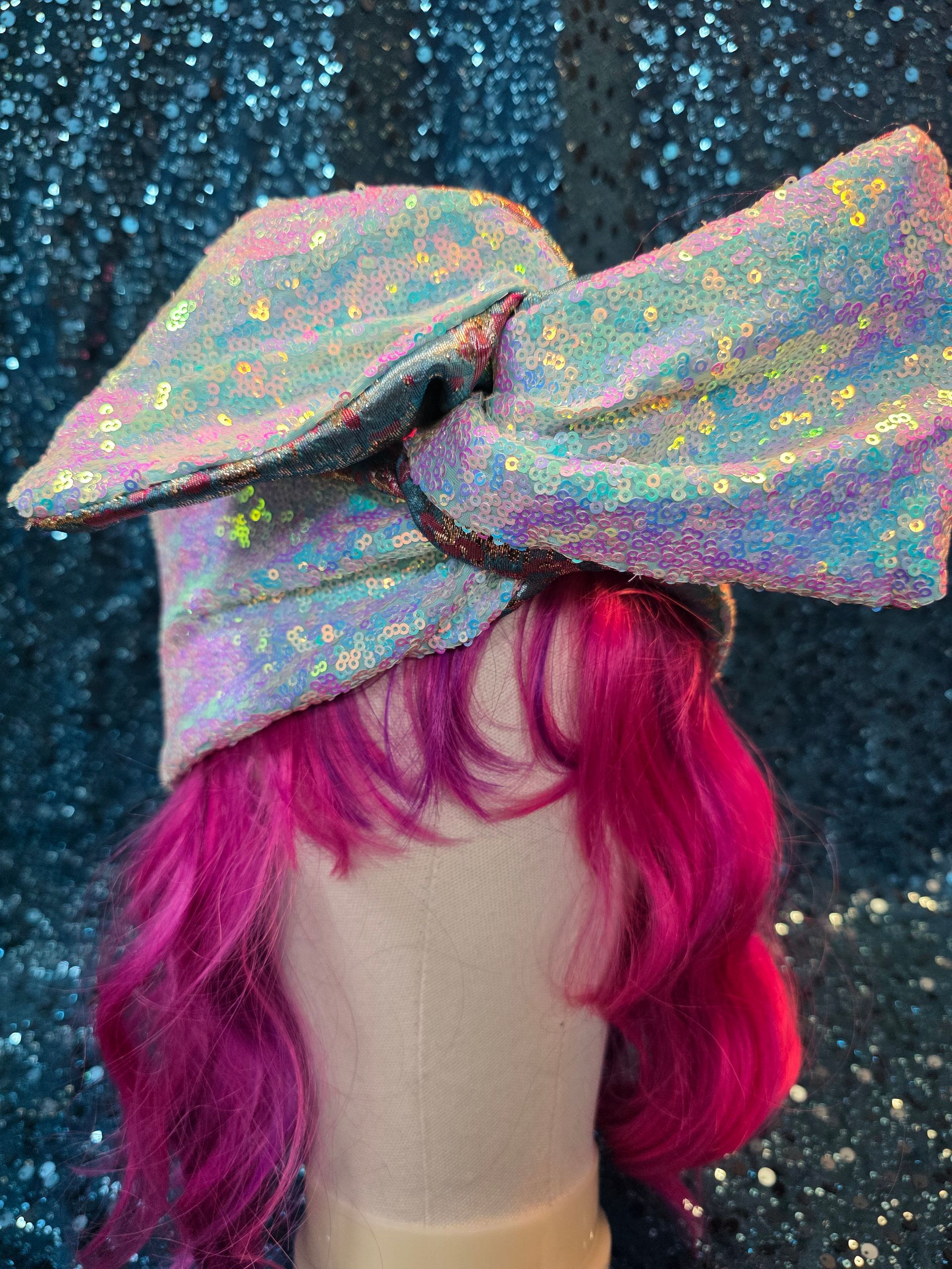 Pastelkleurige hoed met brede rand en glitters op een paspop met felroze haar tegen een glinsterende blauwe achtergrond