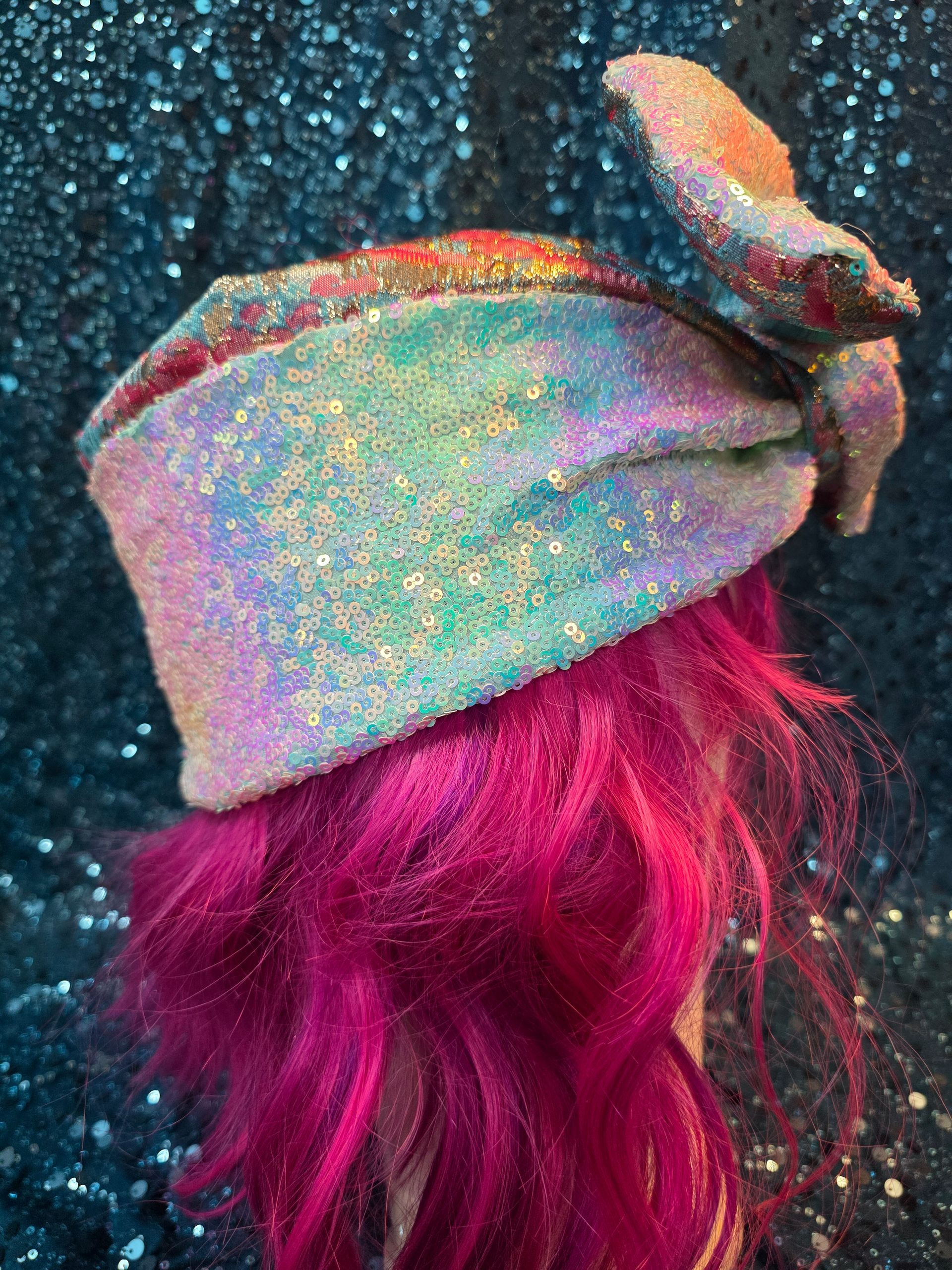 Pastelkleurige hoed met brede rand en glitters op een paspop met felroze haar tegen een glinsterende blauwe achtergrond