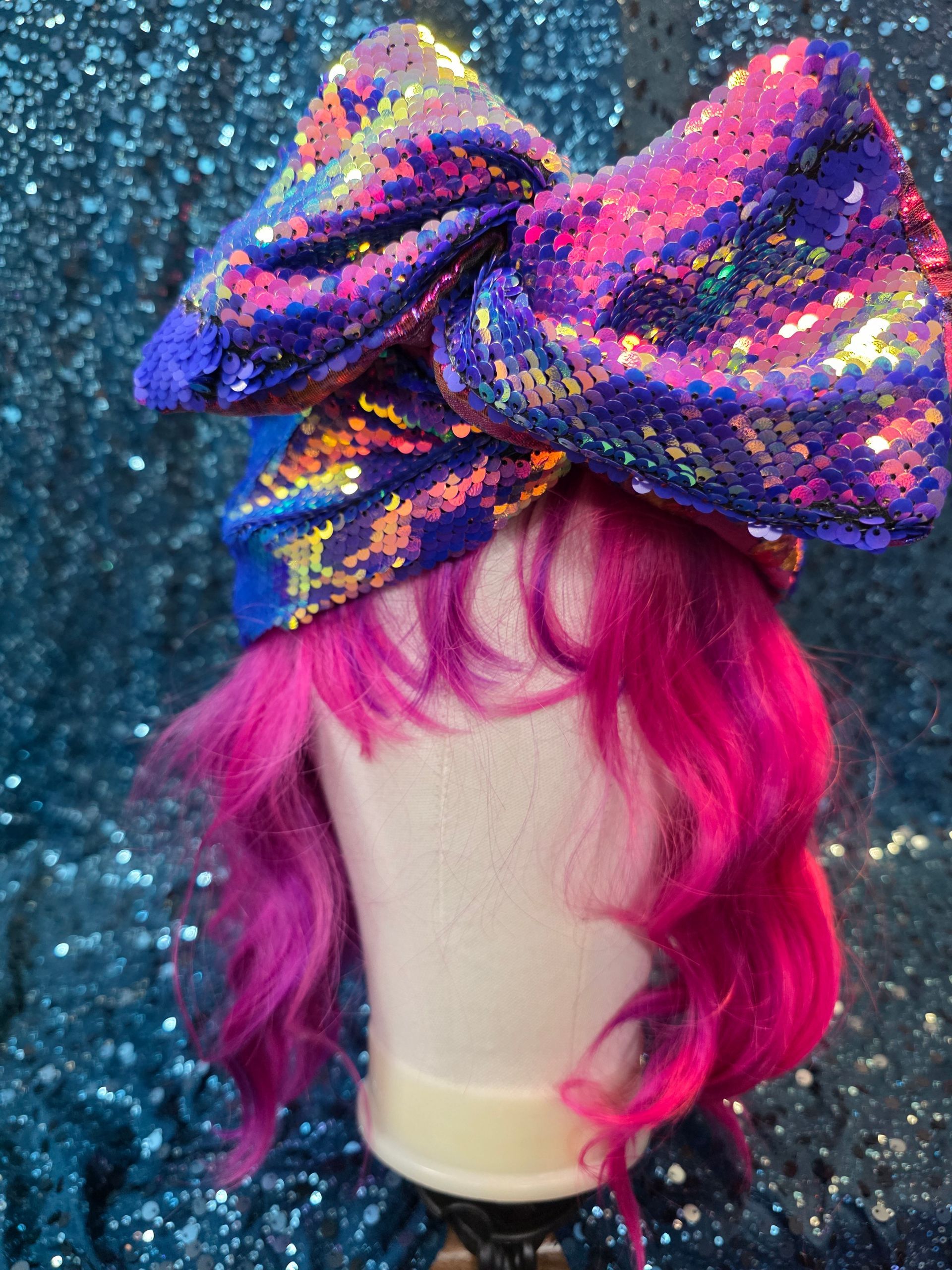 Paspoppenhoofd met een felroze pruik en een grote paarsblauwe strik met pailletten op een glitterende blauwe achtergrond