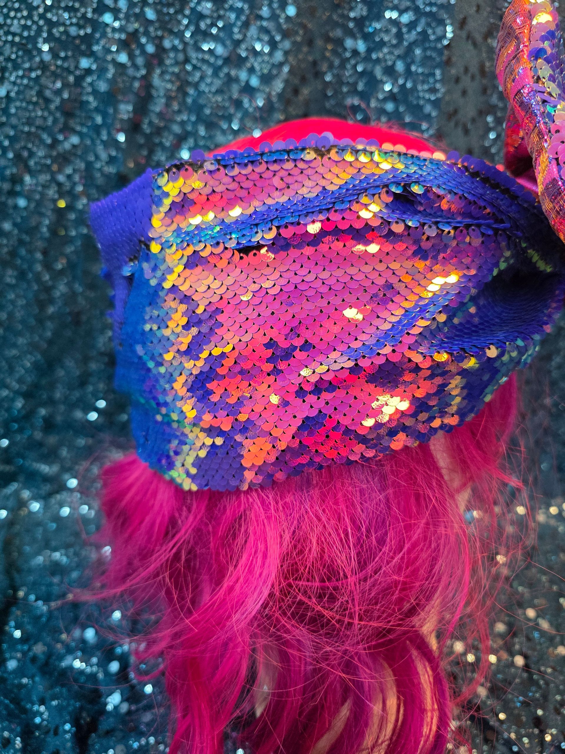 Paspoppenhoofd met een felroze pruik en een grote paarsblauwe strik met pailletten op een glitterende blauwe achtergrond