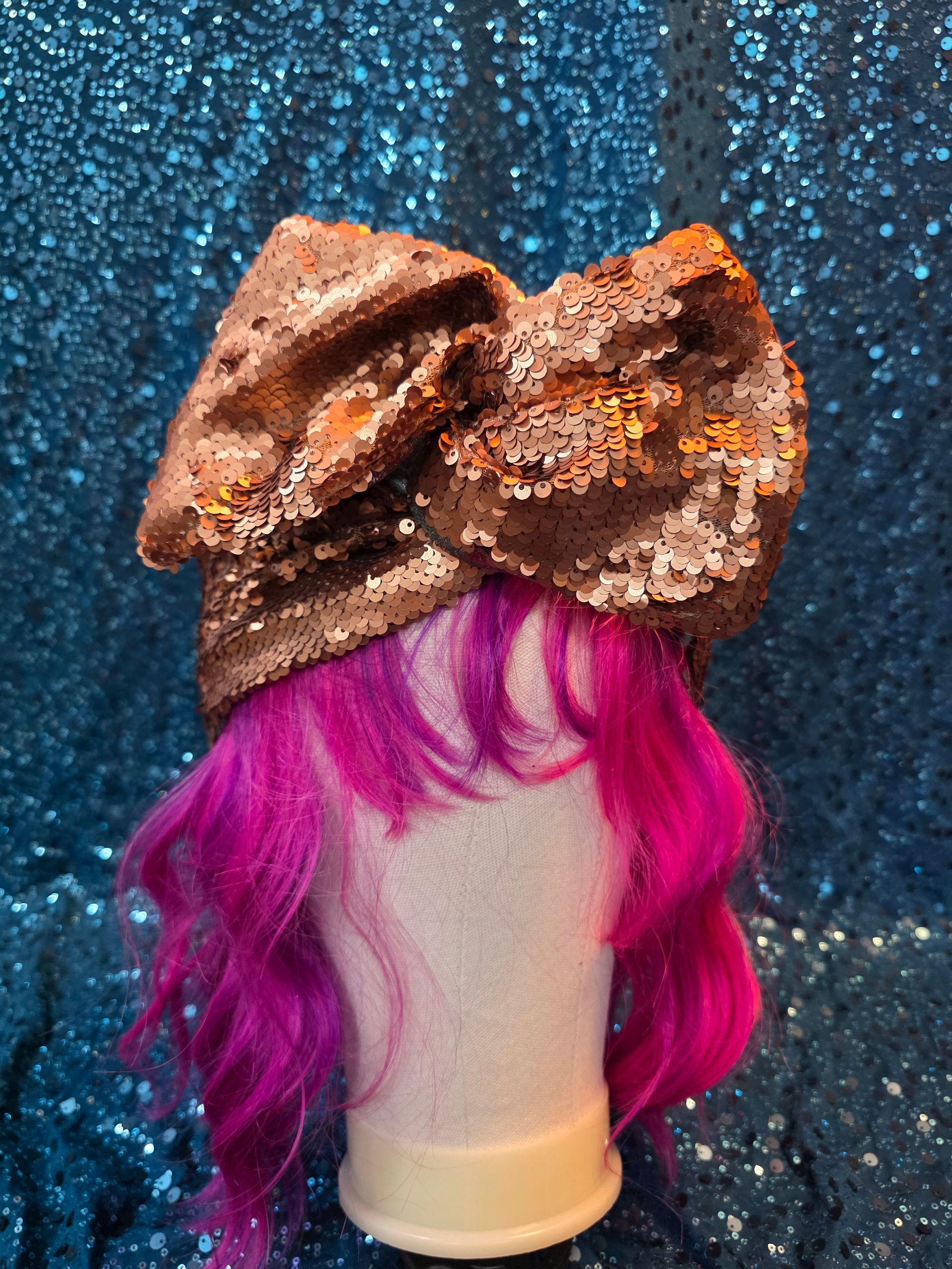 Etalagepoppenhoofd met felroze haar en een grote bruine strik tegen een glitterende blauwe achtergrond