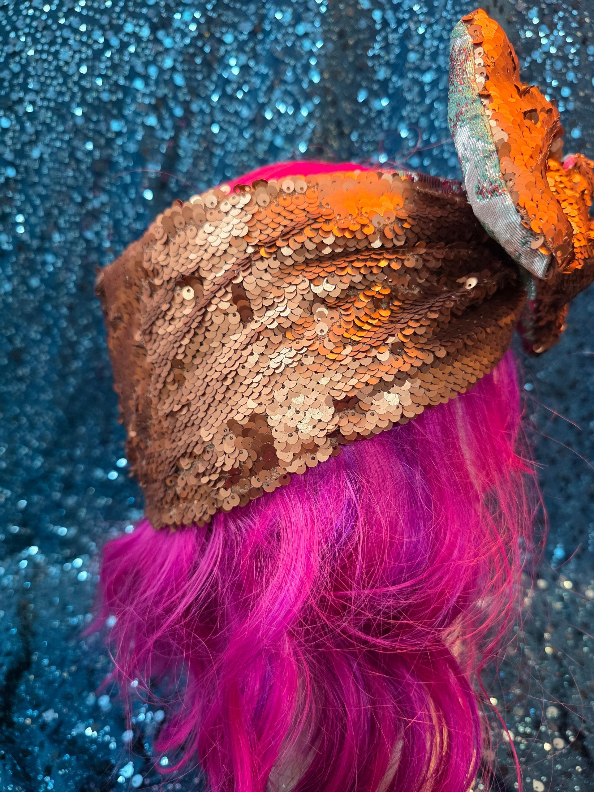 Etalagepoppenhoofd met felroze haar en een grote bruine strik tegen een glitterende blauwe achtergrond