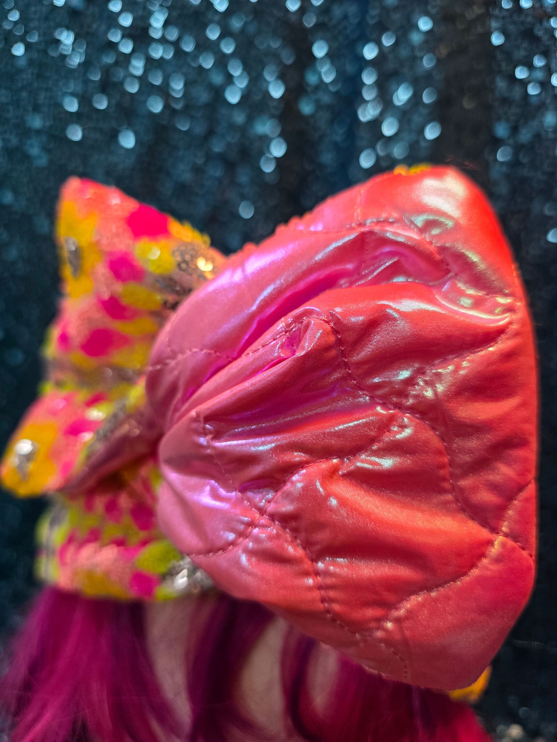 Magenta pruik op een paspophoofd met een kleurrijke bloemenstrik tegen een sprankelende blauwe achtergrond