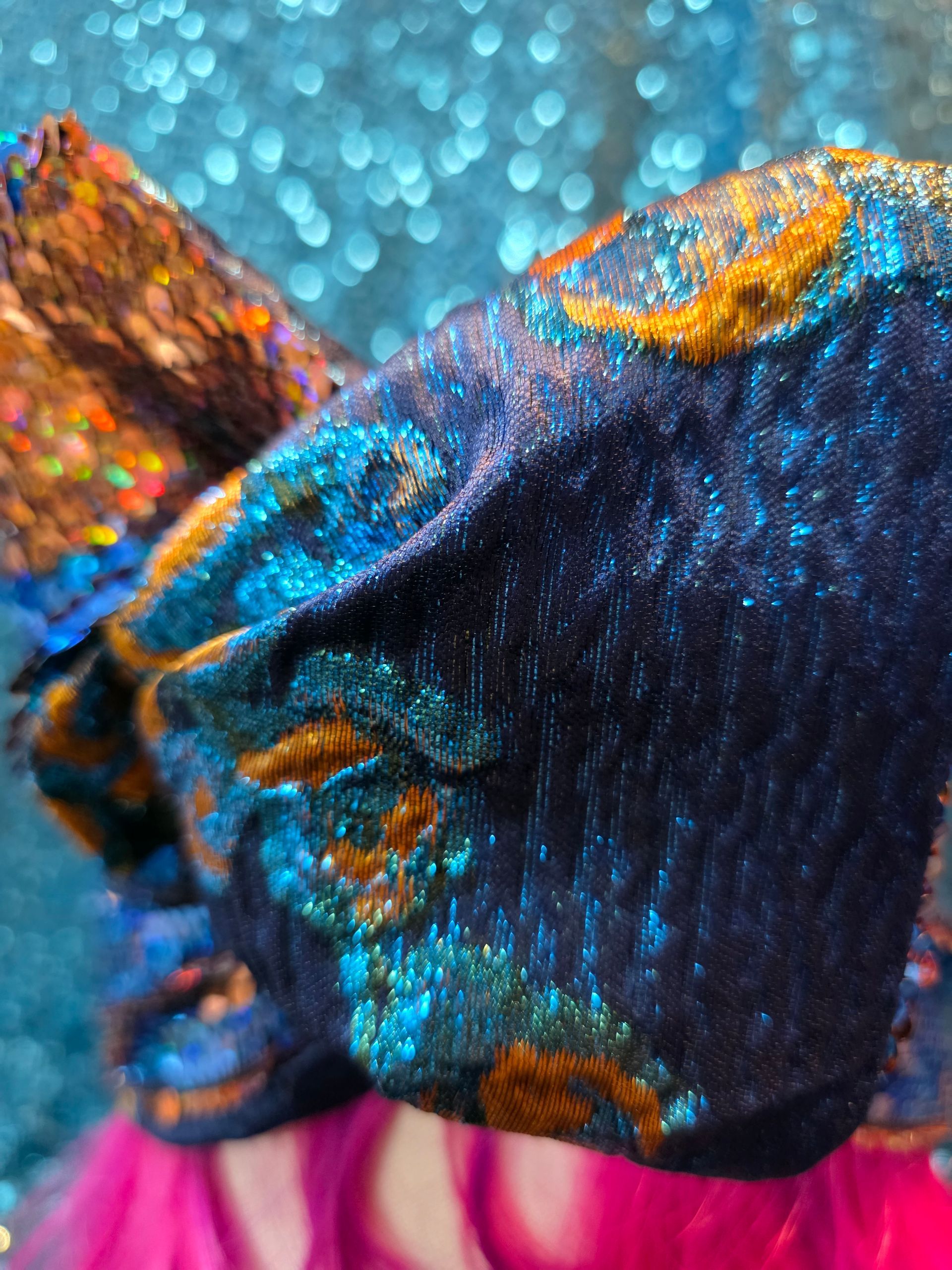 Felroze pruik met een blauwe strik met lovertjes op een paspophoofd tegen een glitterende blauwe achtergrond