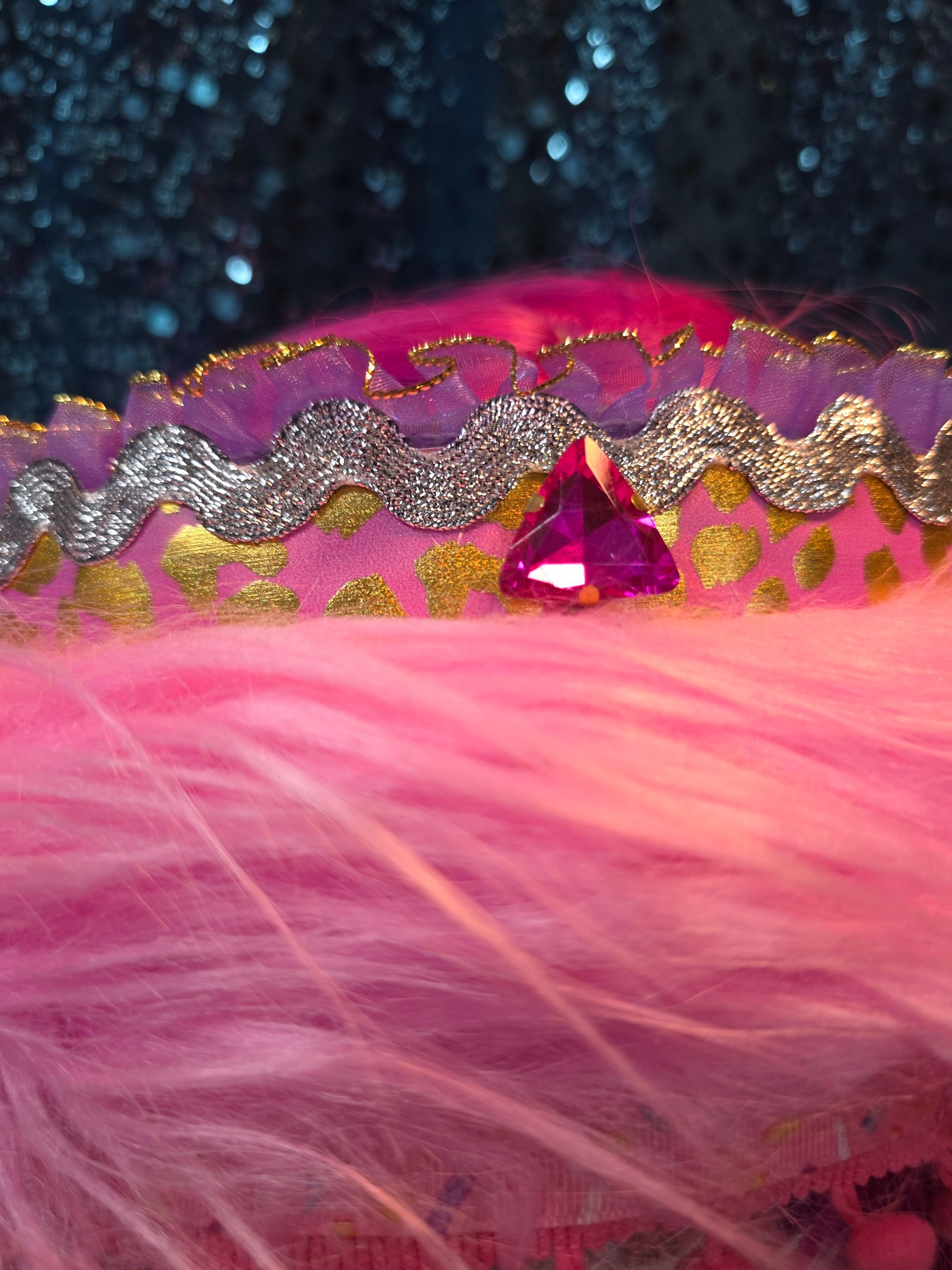 Etalagepoppenhoofd met een roze hoed met veren en paarse kralensnoeren tegen een glinsterende blauwe achtergrond