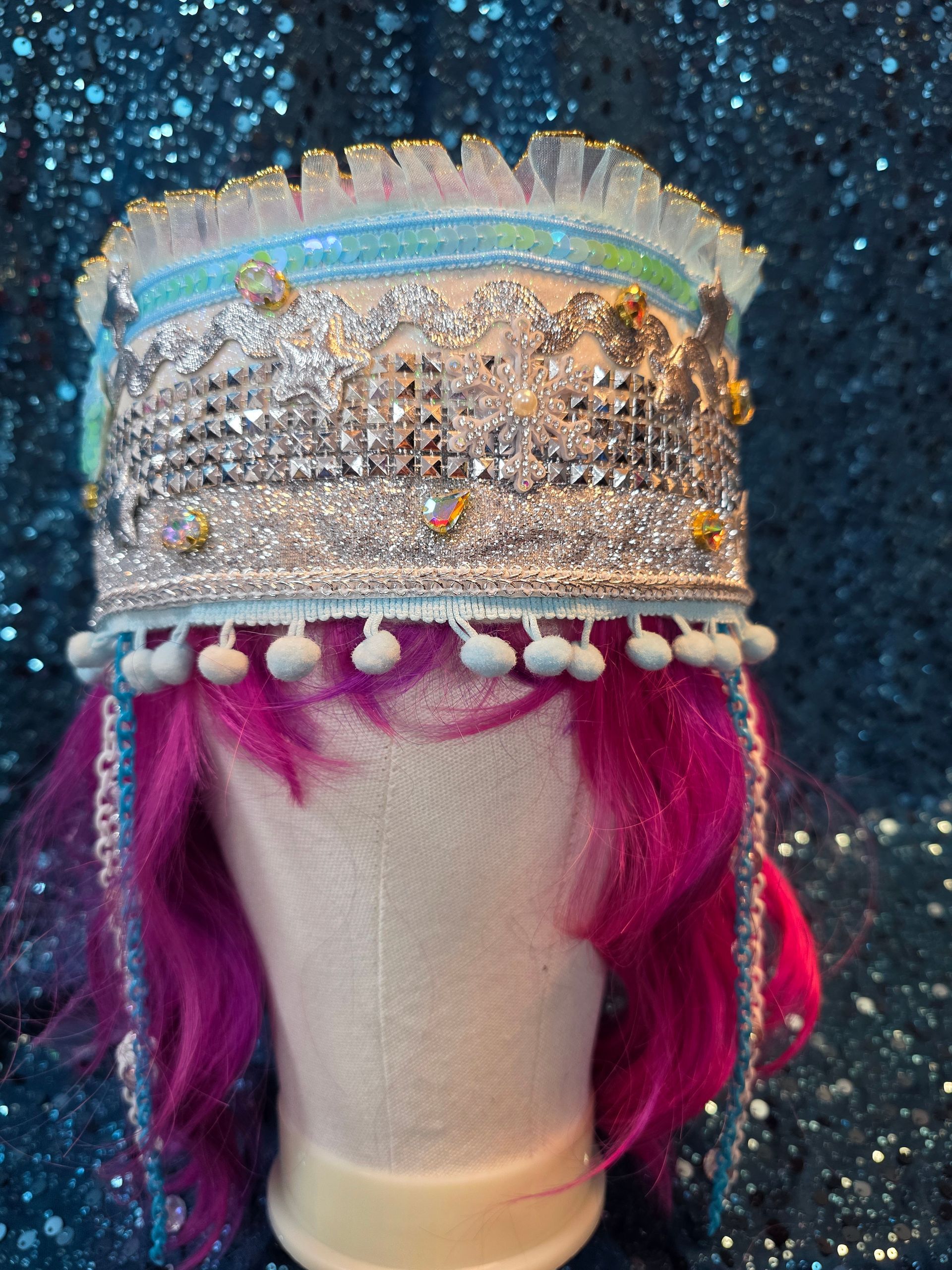 Etalagepophoofd met een zilveren, met juwelen versierde hoofdtooi en roze haar tegen een glitterende blauwe achtergrond