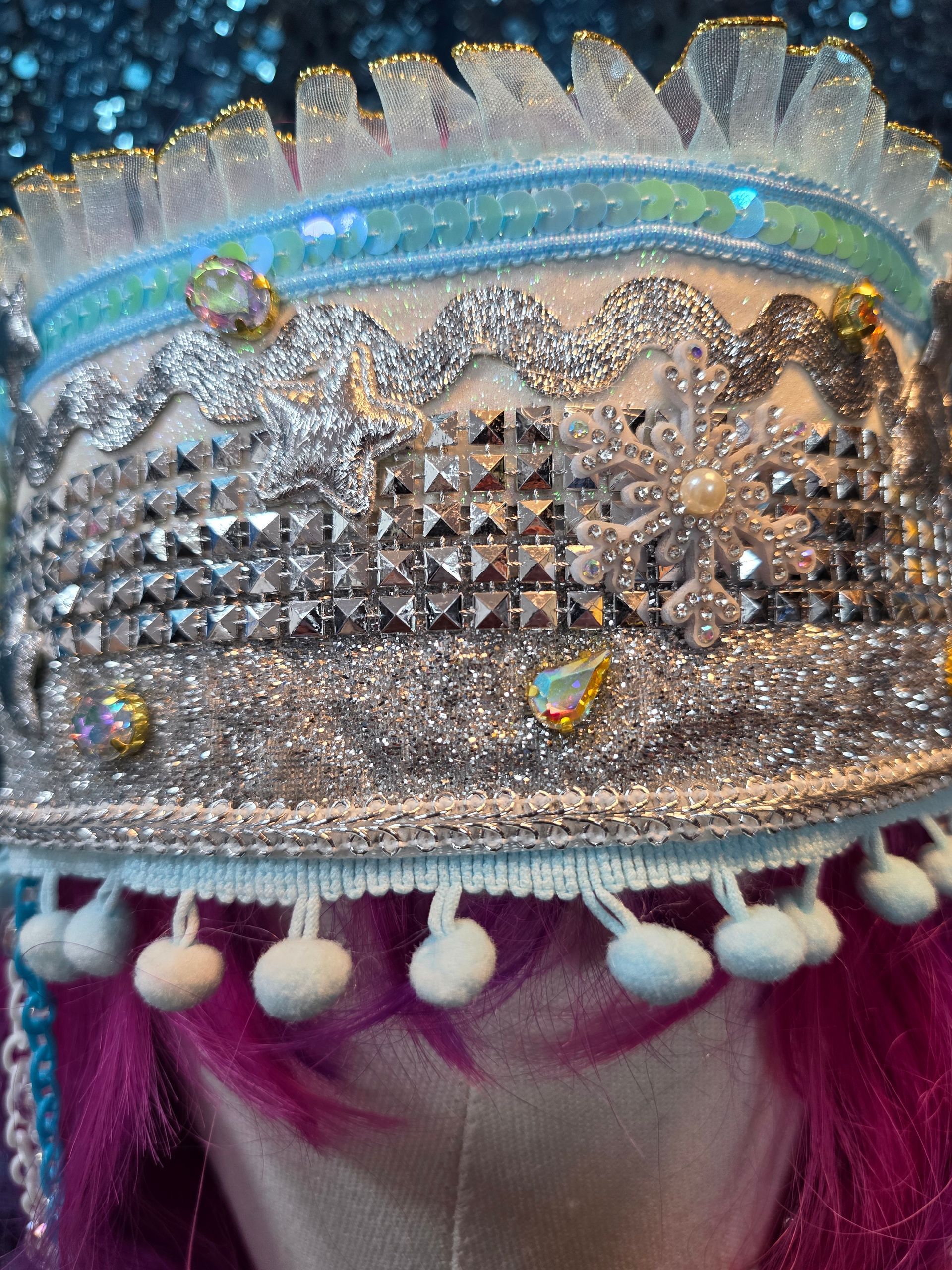 Etalagepophoofd met een zilveren, met juwelen versierde hoofdtooi en roze haar tegen een glitterende blauwe achtergrond