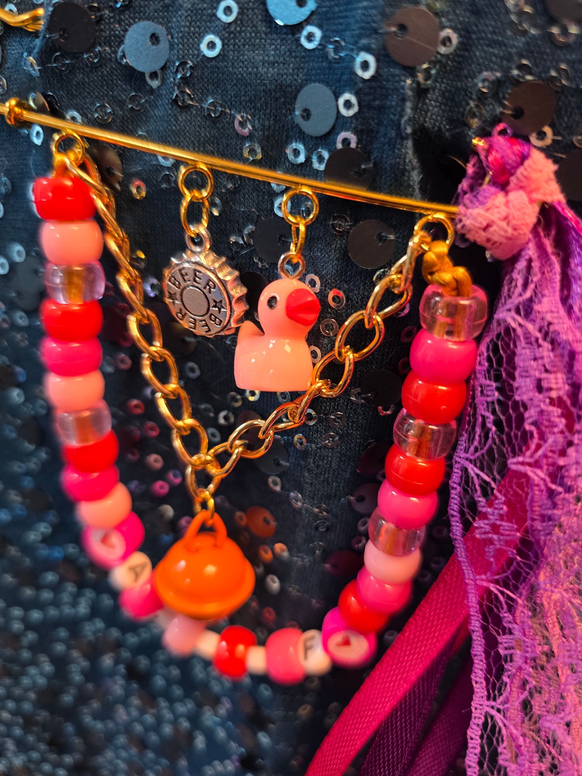 Kleurrijke kralenkettingen met bedeltjes en een roze kwastje op donkere stof met pailletten