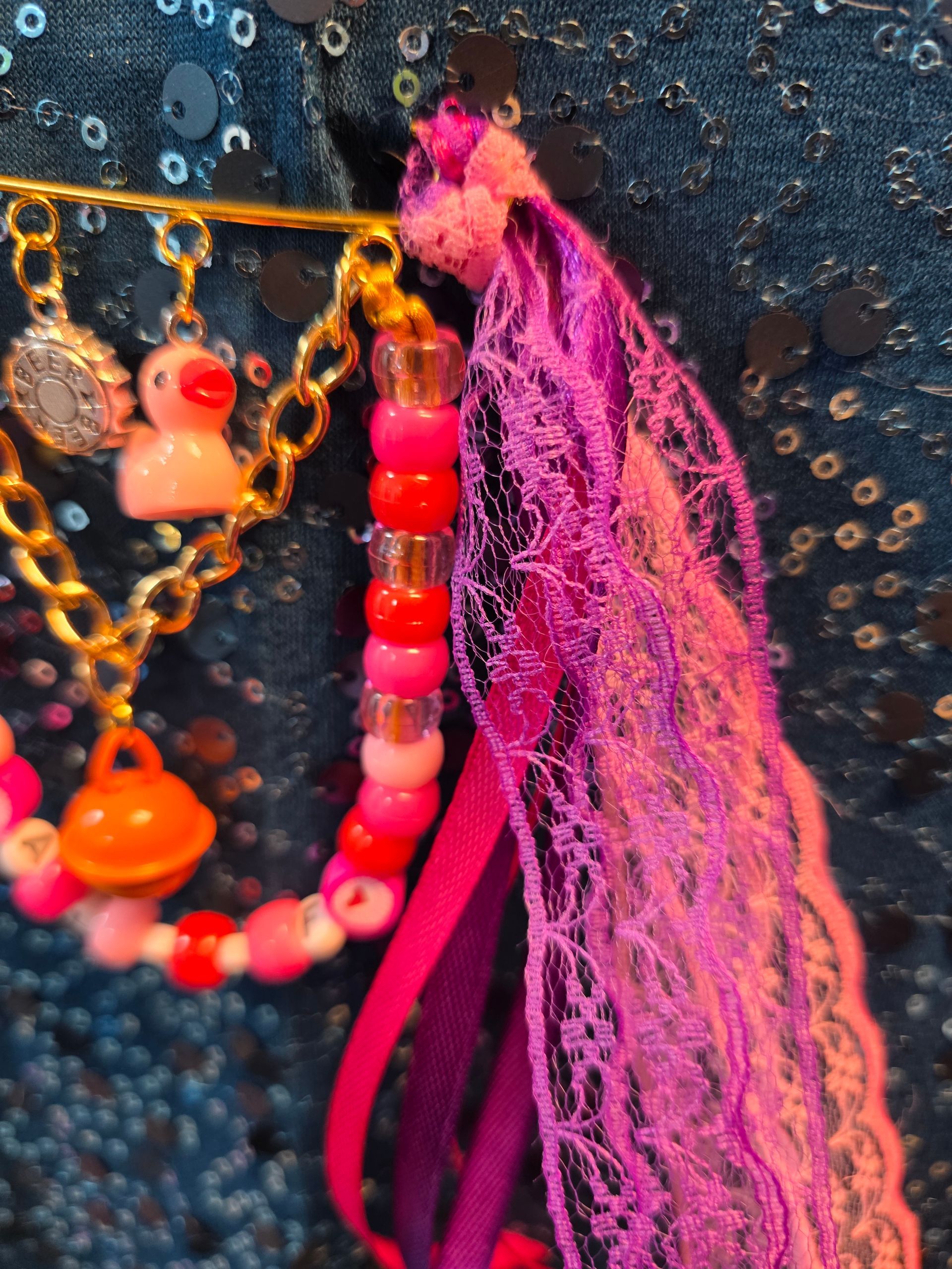 Kleurrijke kralenkettingen met bedeltjes en een roze kwastje op donkere stof met pailletten