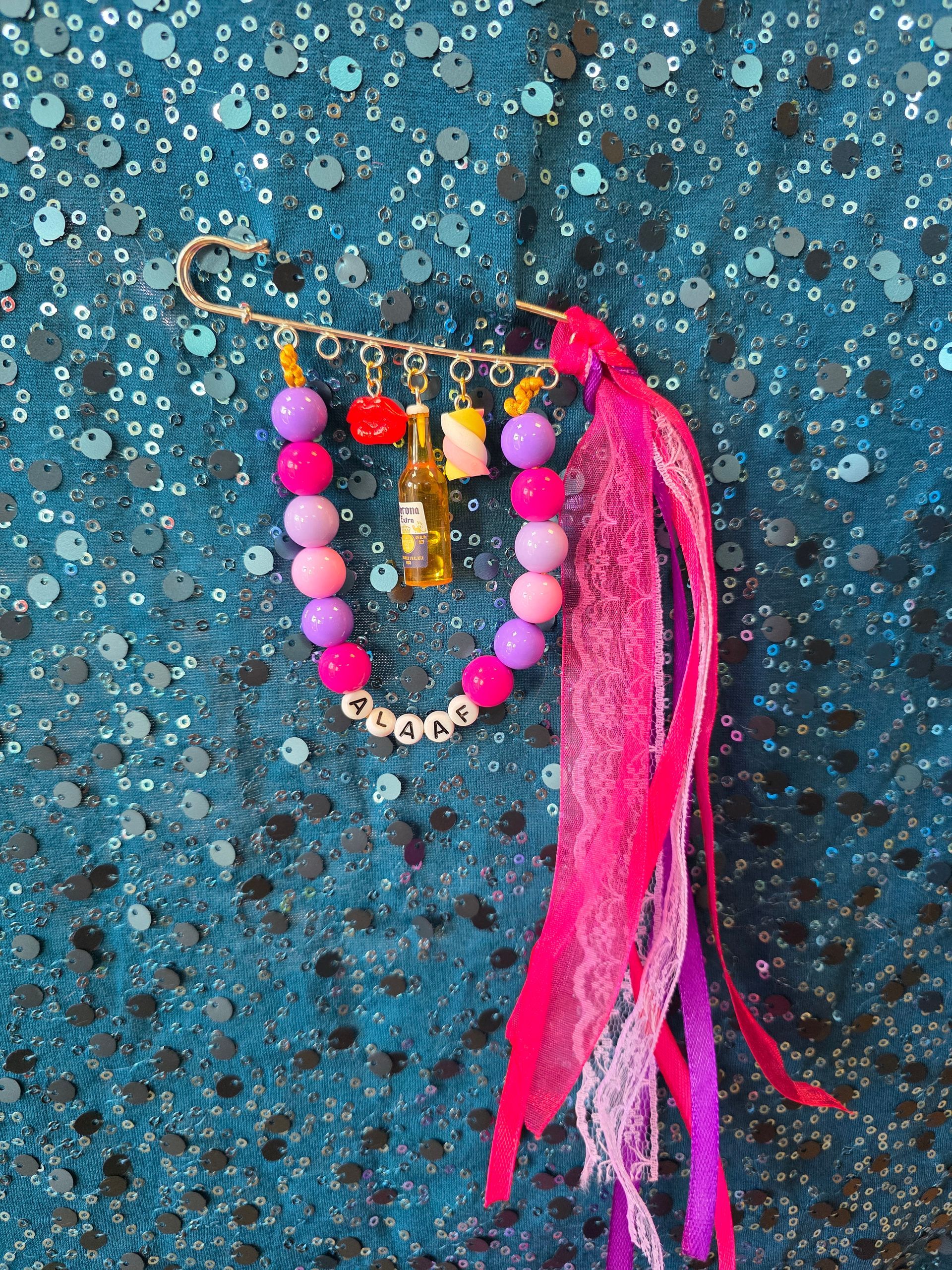 Roze sleutelhanger met kwastje en kralen, hangend tegen een turkooizen achtergrond met textuur