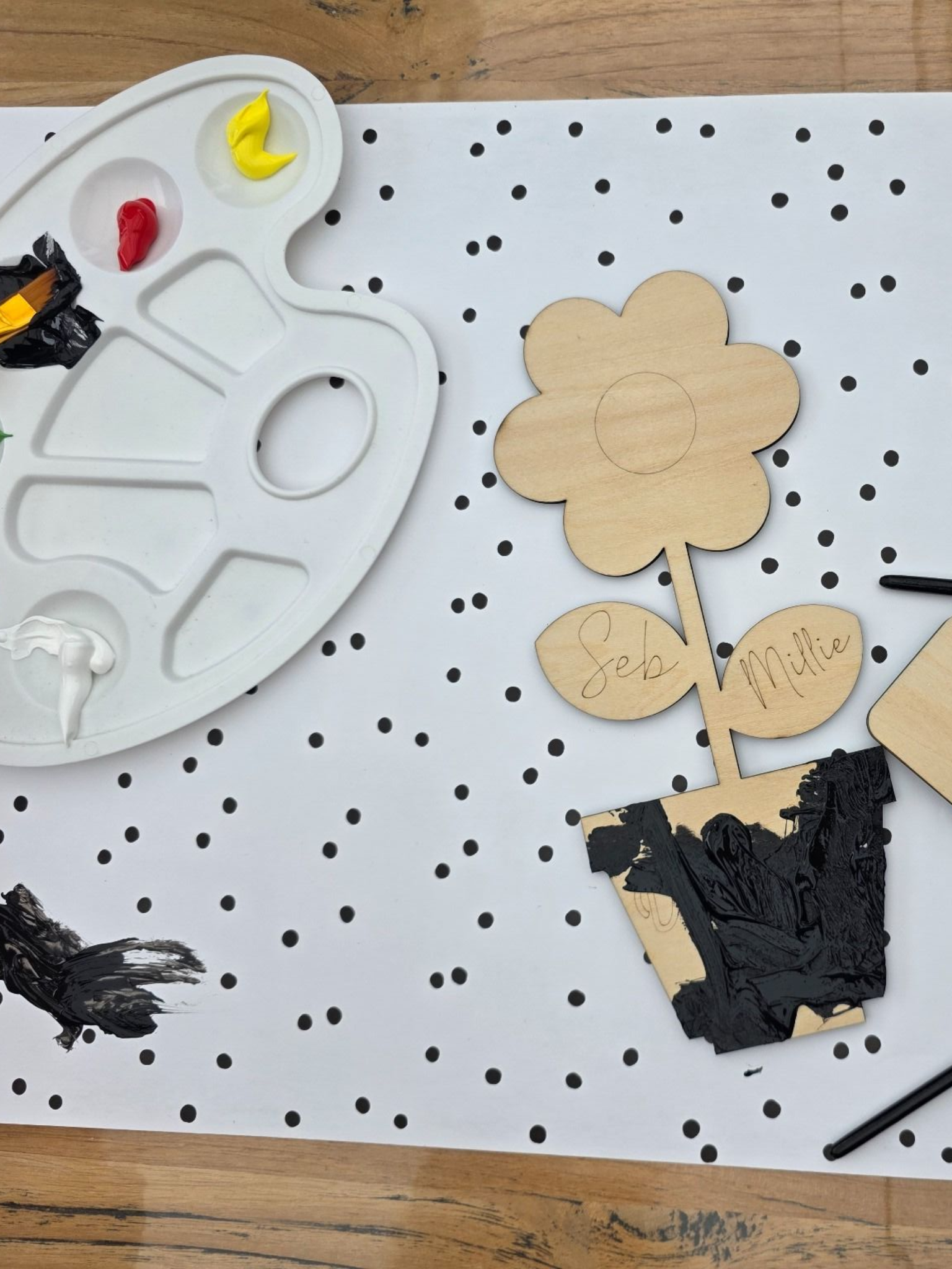 Twee decoratieve houten bloembordjes in potjes, waarvan één kleurrijk beschilderd en de andere onafgewerkt, op een tafelblad.