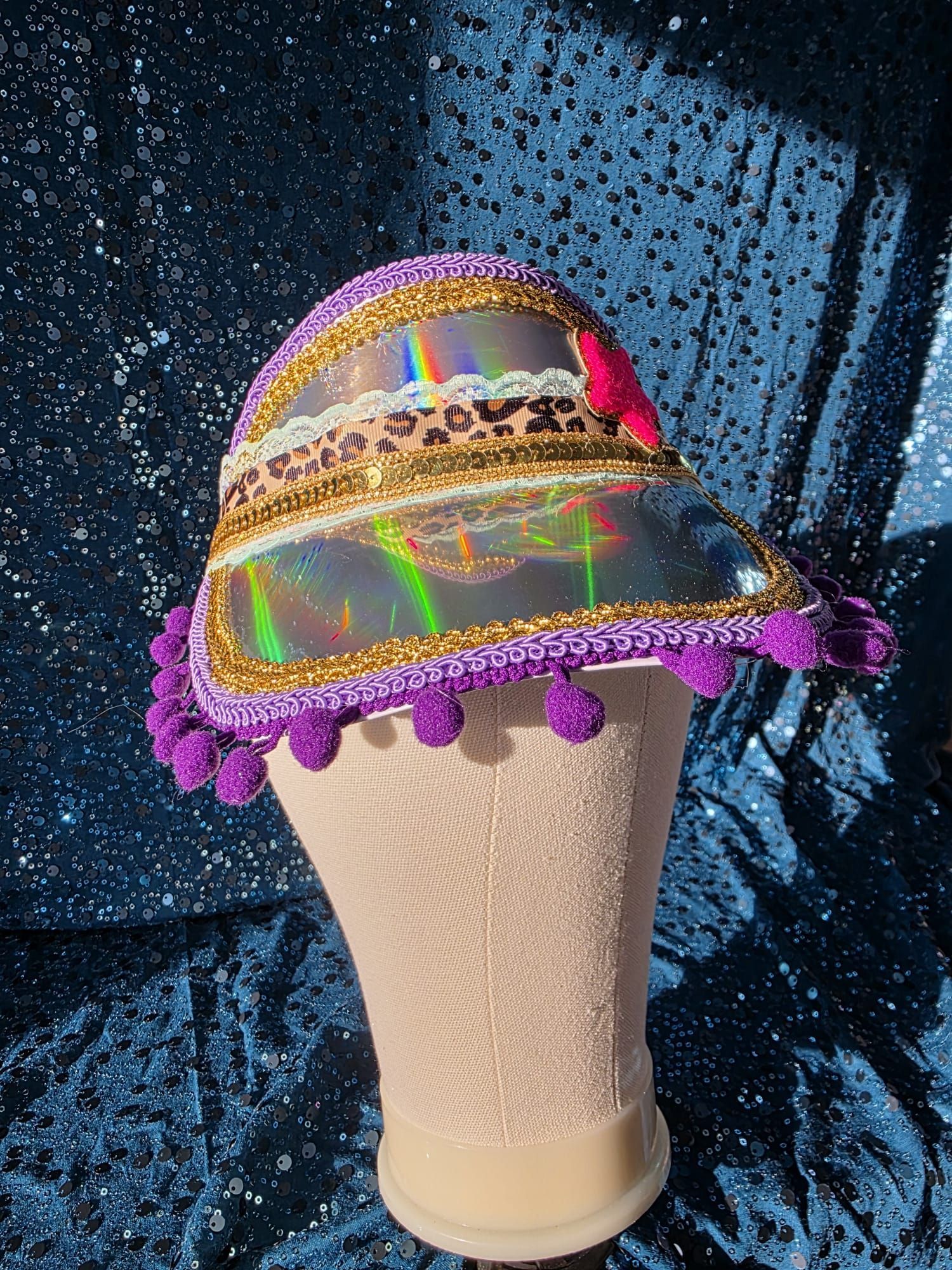 Decoratief ijshoorntje met een iriserende regenboogmuts en paarse pompons op een glinsterende blauwe achtergrond.