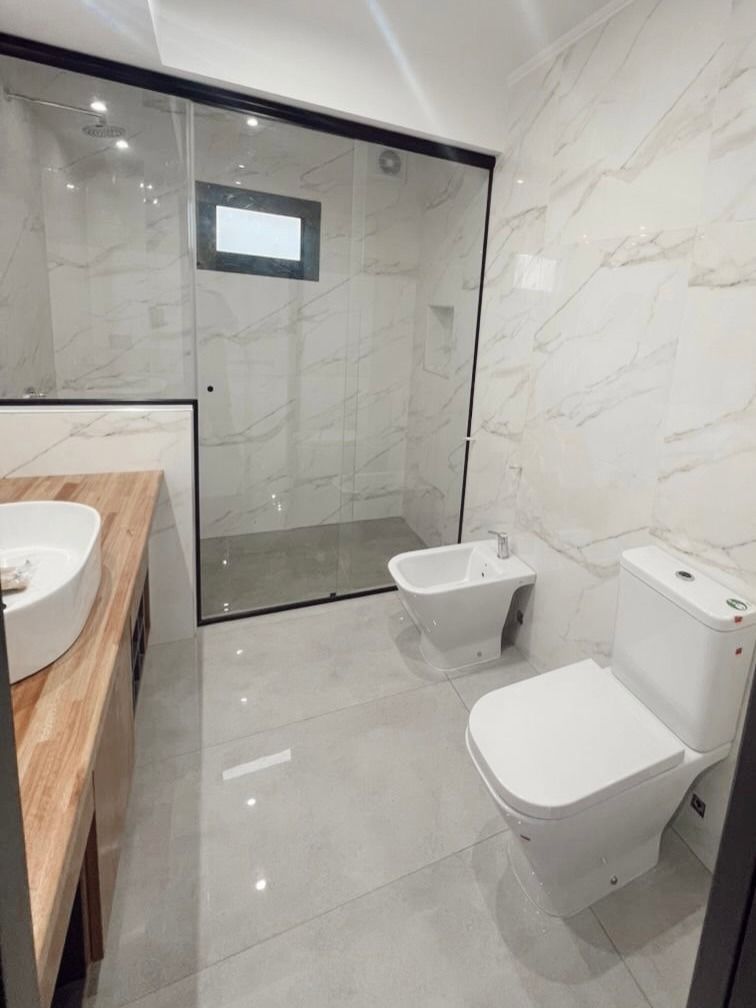 Baño moderno con ducha de cristal, inodoro, bidé mural y lavabo de madera.
