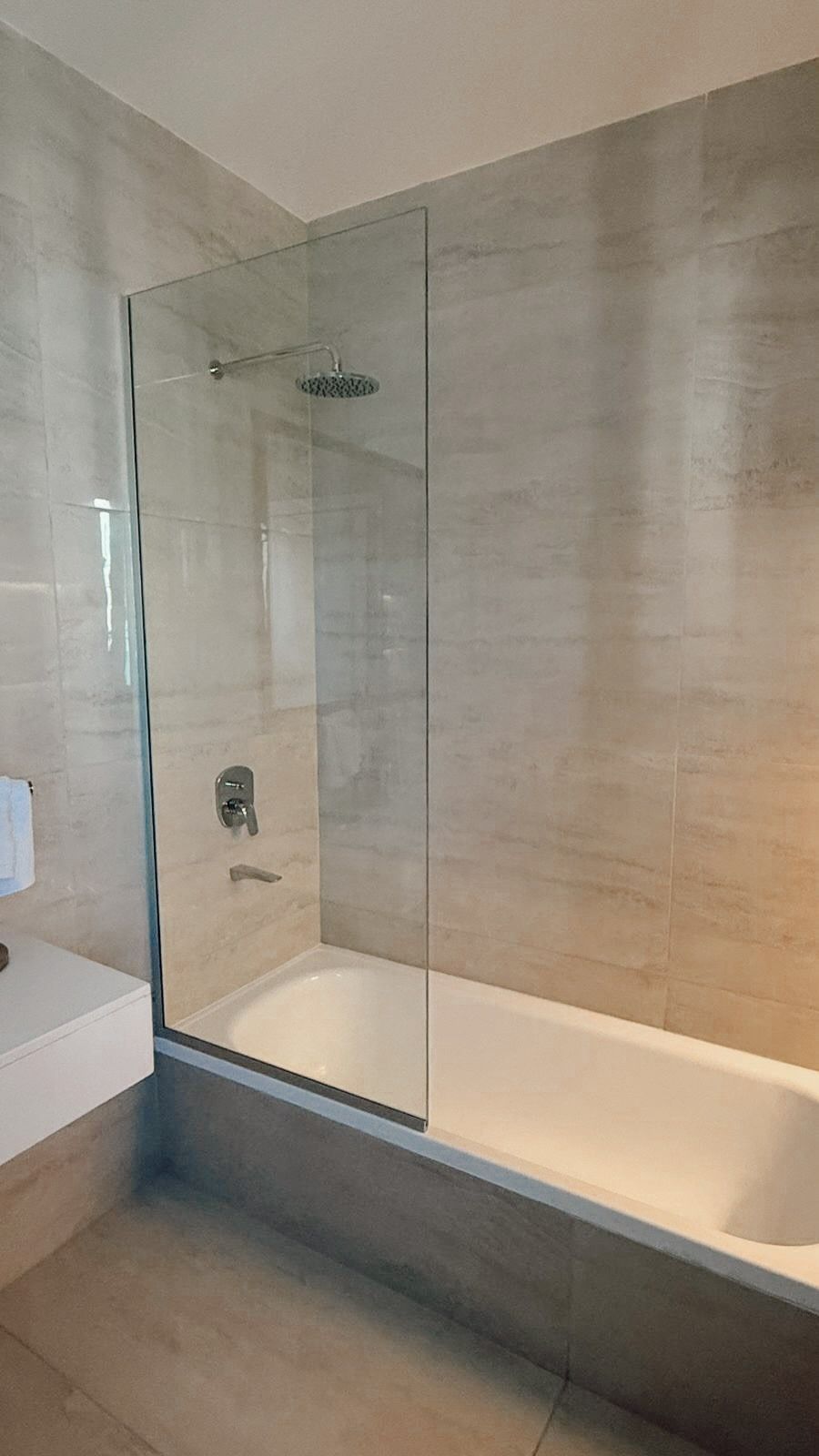 Baño moderno con bañera con cerramiento de cristal y paredes alicatadas en color beige.