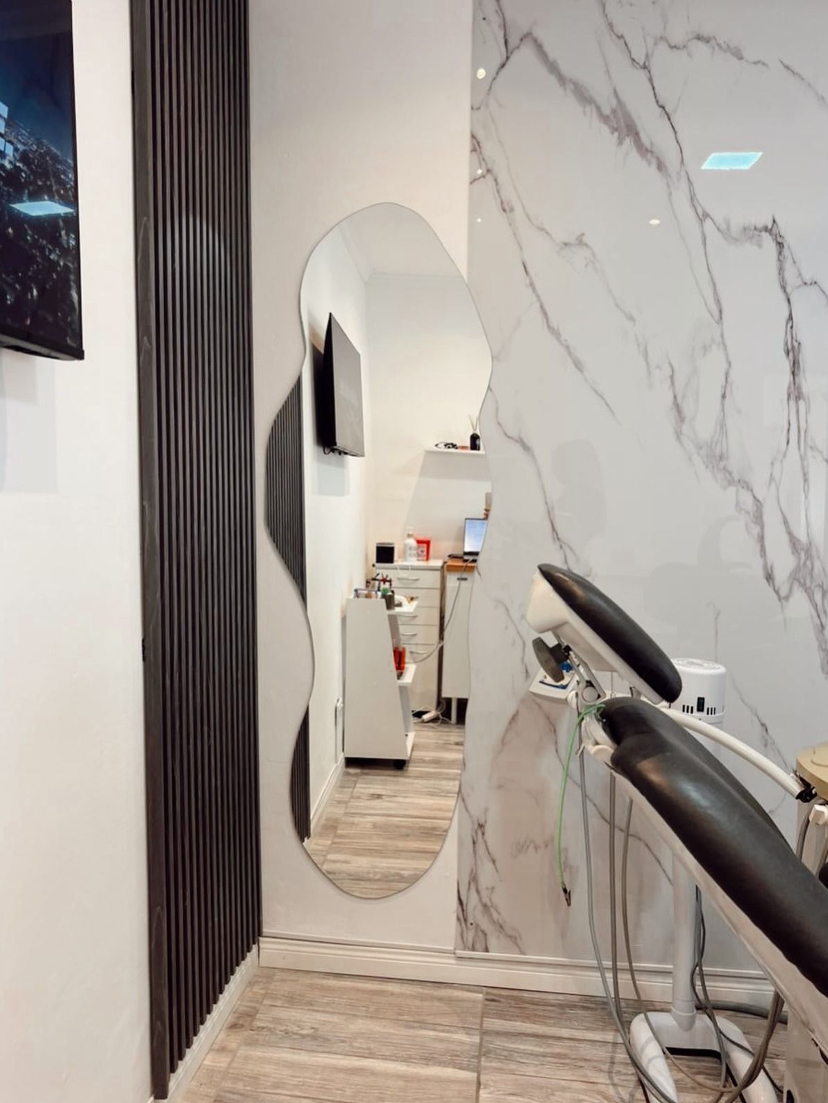 Interior del salón con espejo de pared ondulado, pared decorativa de mármol y sillón reclinable para tratamientos.