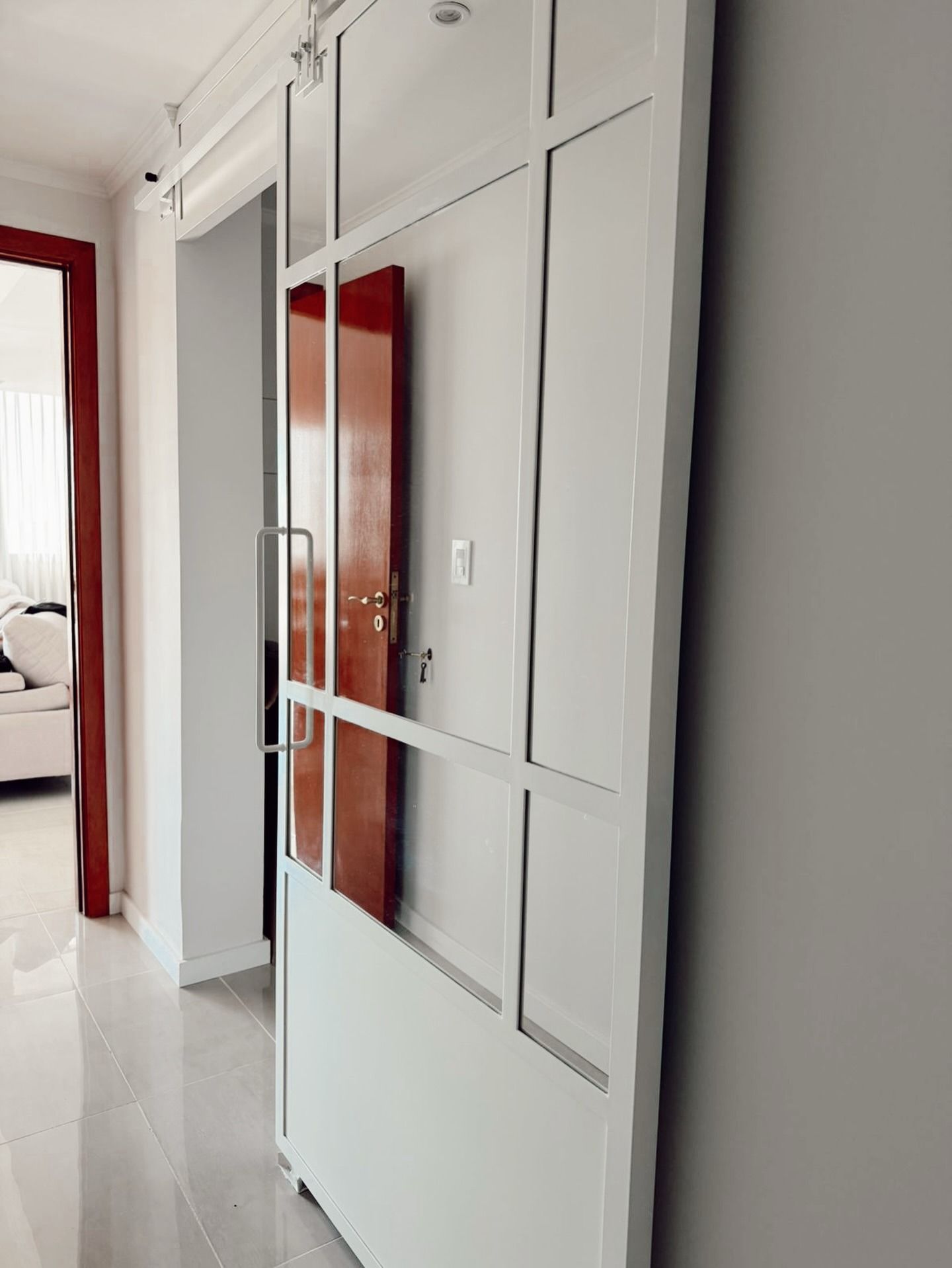 Pasillo con puertas correderas blancas en el armario y un espejo con marco rojo que refleja un dormitorio.