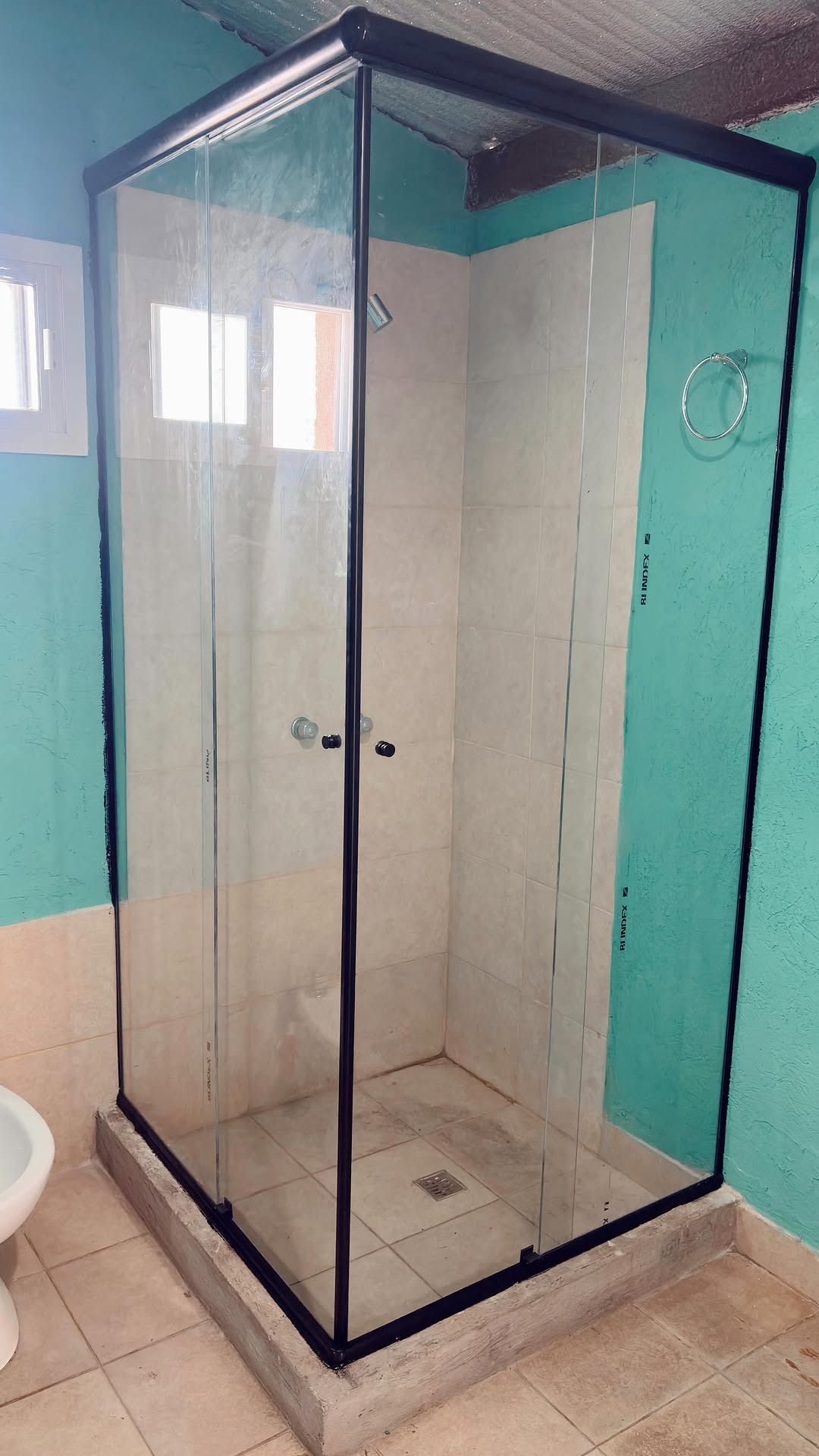Mampara de ducha de cristal en esquina con marco negro en un baño turquesa.